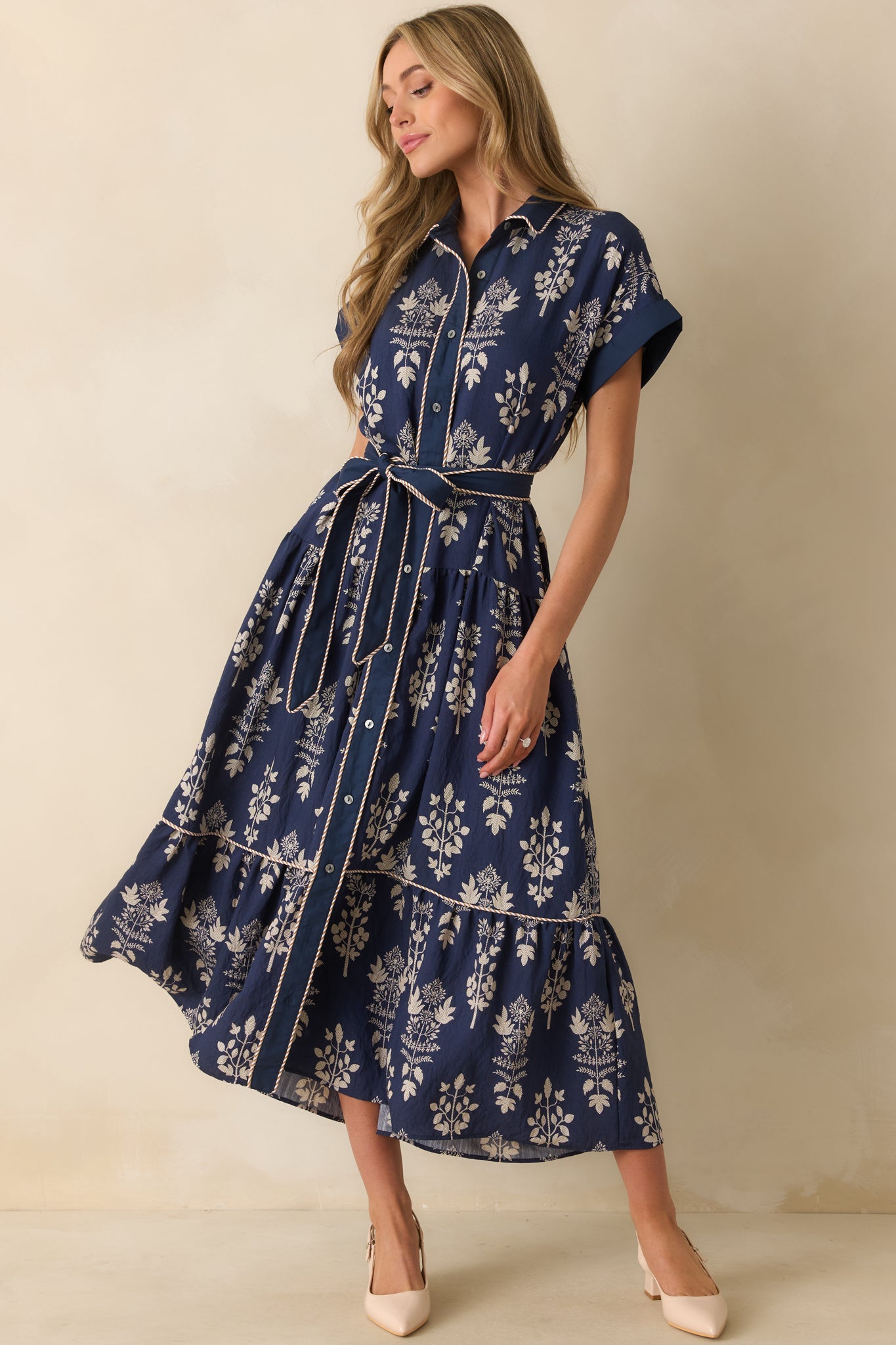 Flowing navy maxi dress with ivory floral print, short cuffed sleeves, collared neckline, and a self-tie belt at the waist.