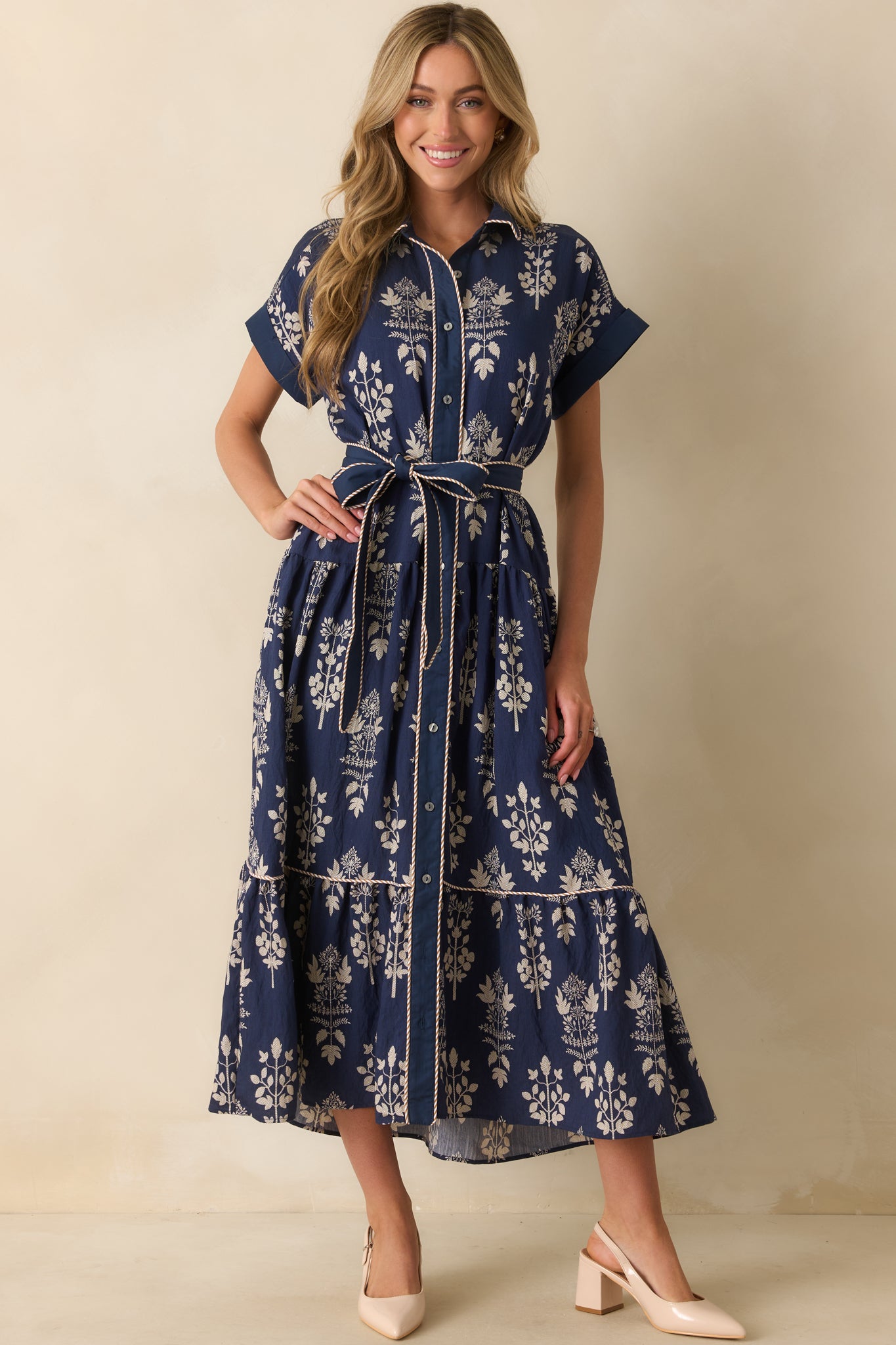 Navy maxi dress with ivory floral print, collared neckline, short cuffed sleeves, and a tiered skirt.