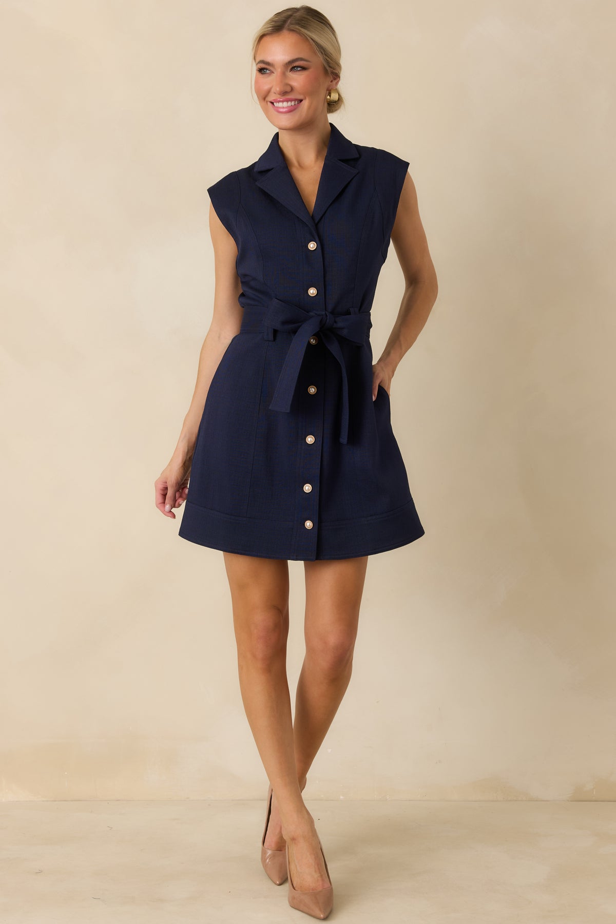 Navy A-line mini dress with gold-accented pearl buttons, structured shoulders, side pockets, and a defined belted waist.