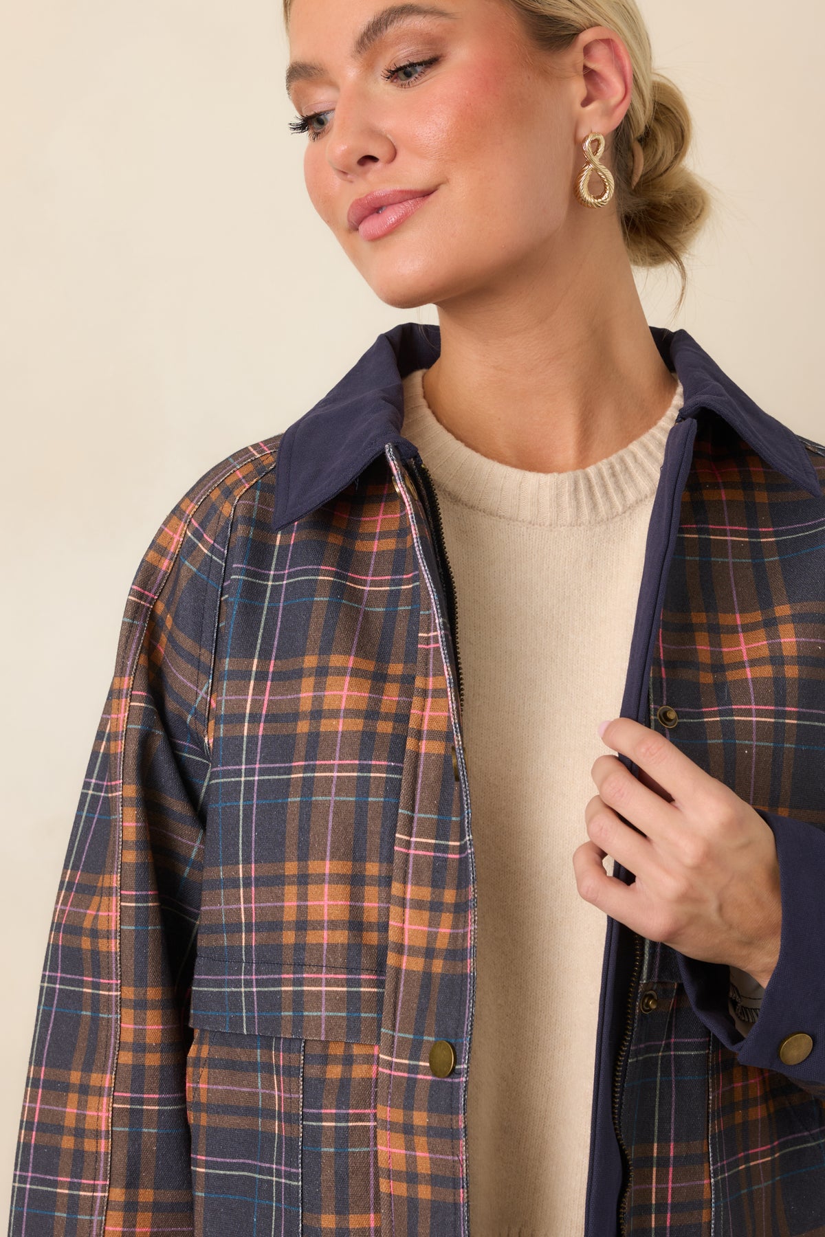 Close view of the navy plaid pattern, solid trim, zipper, snap placket, and layered storm-flap detailing.