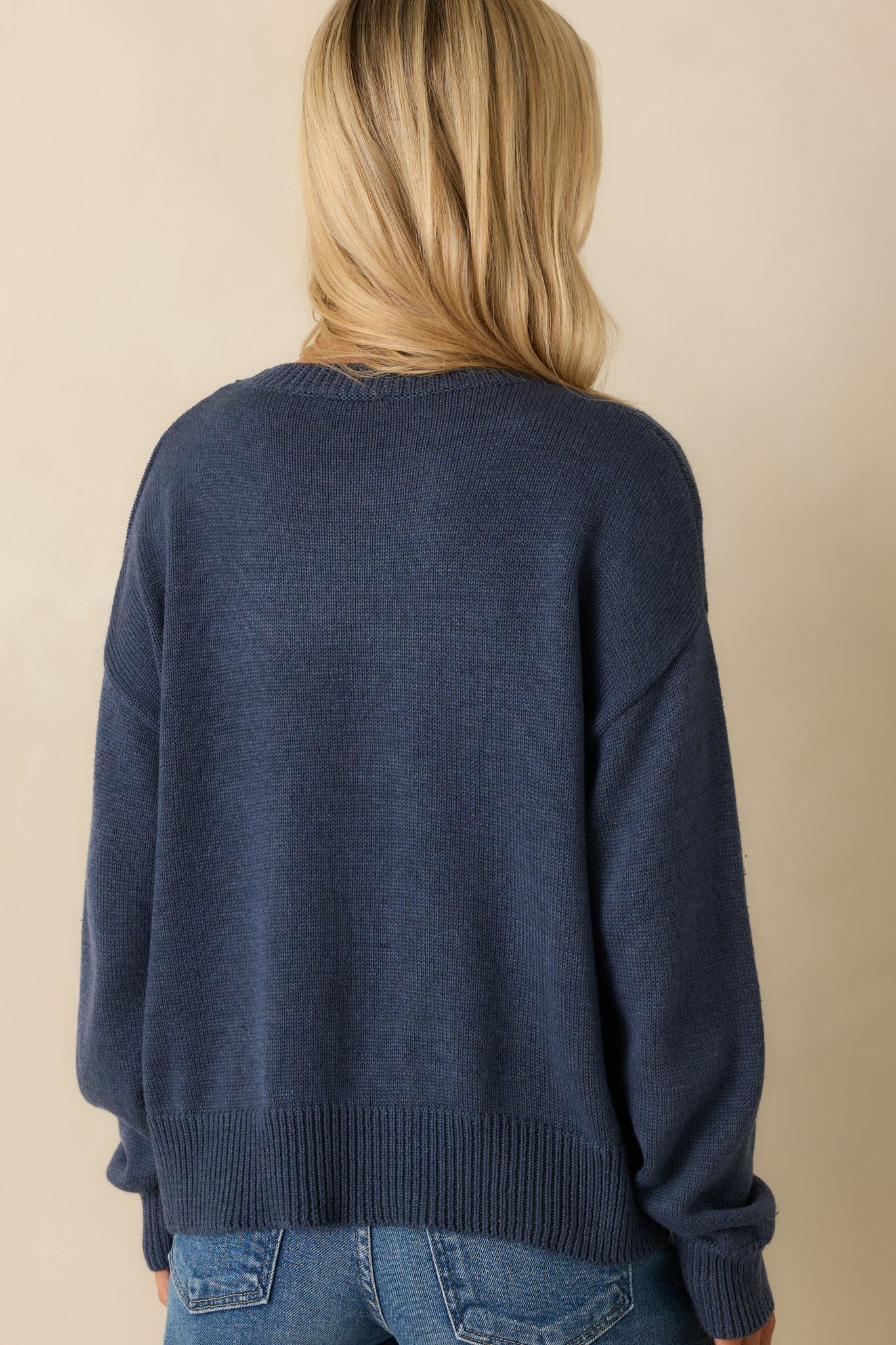 Back view of navy pullover sweater showing smooth knit fabric, ribbed cuffs, and relaxed fit silhouette.