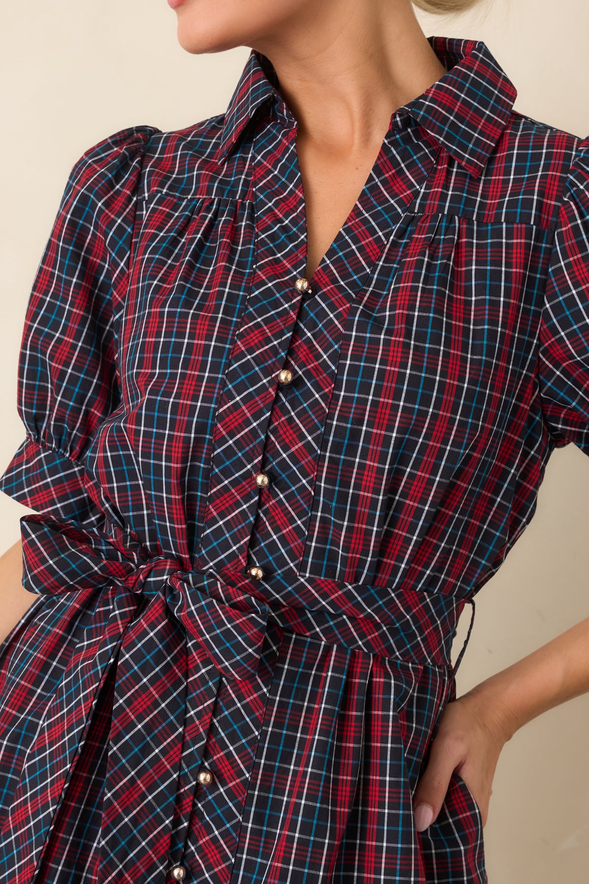 Close-up detail of the navy and red plaid dress showing its gold-tone buttons, collar, and softly gathered sleeve.