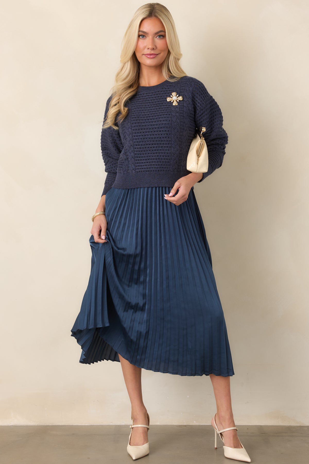 Navy two-piece set featuring a cropped open-knit sweater over a sleeveless satin midi dress with a flowy pleated skirt.