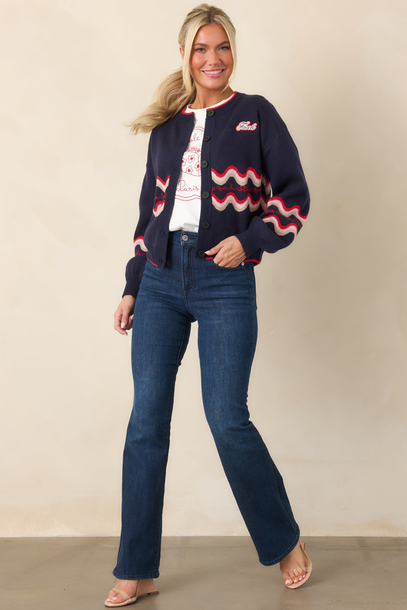Relaxed-fit navy cardigan showcasing bold red and cream wave patterns, long sleeves, contrast red edging, and a small logo patch at the chest.
