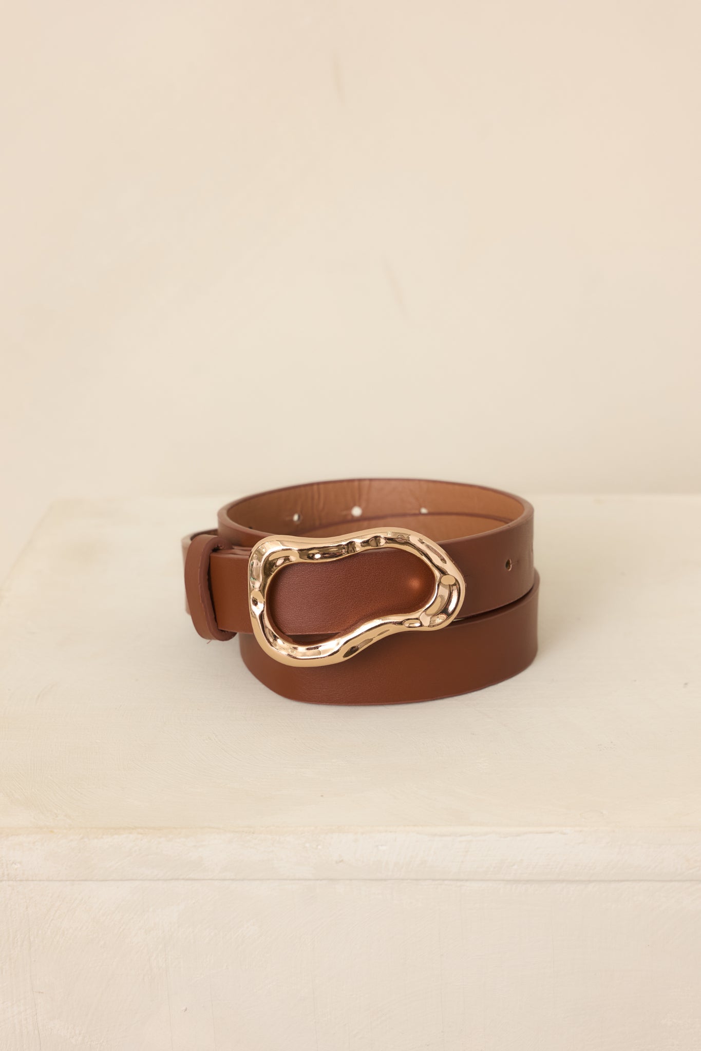 Neutral-toned belt with a flexible structured strap, distinctive sculpted gold-tone buckle, and clean adjustment detailing for a polished finish.