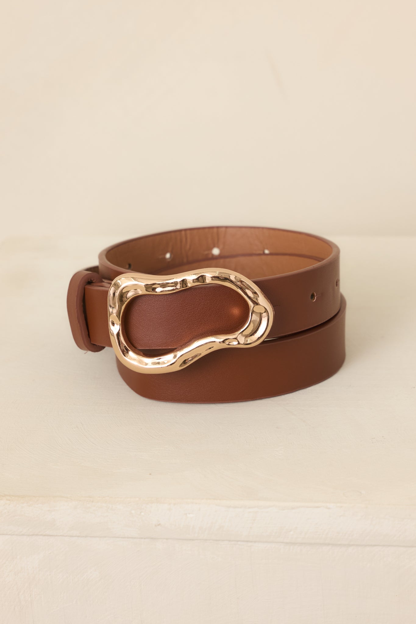 Close-up of the neutral belt highlighting the organic sculpted gold-tone buckle and its polished dimensional finish.