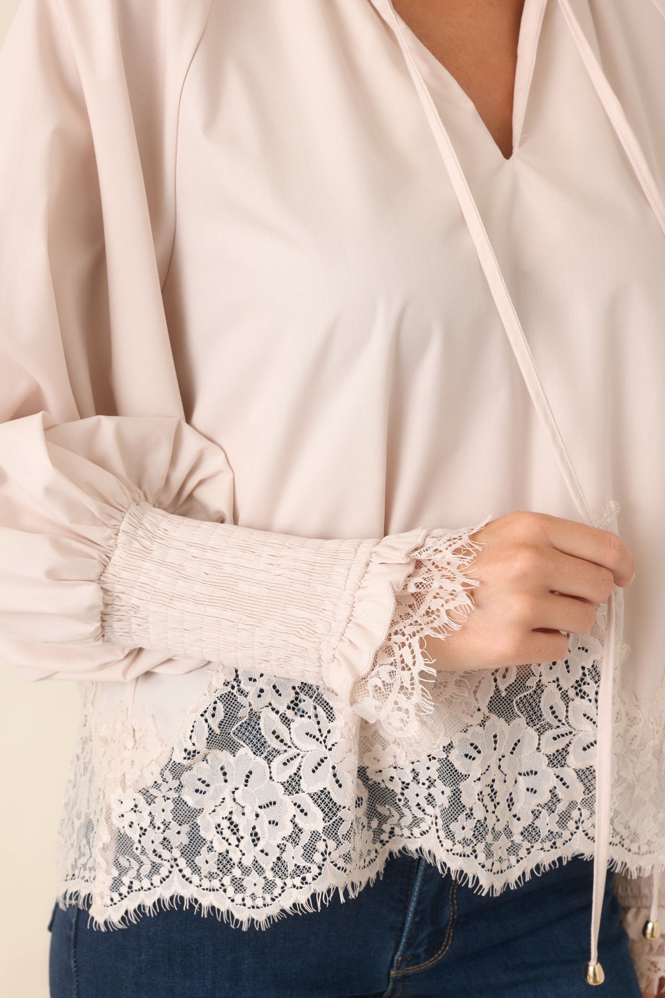 Close-up of the blouse showcasing the ruffled split neckline, polished gold-tone tie tips, delicate lace trim, and beautifully textured floral lace hem against the smooth woven fabric.