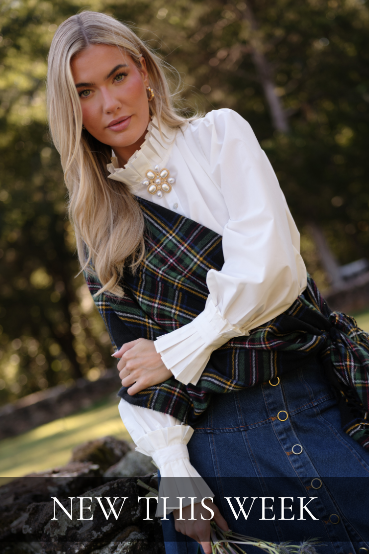 Model wearing a white blouse with a plaid scarf over it. Text reads: "New This Week."