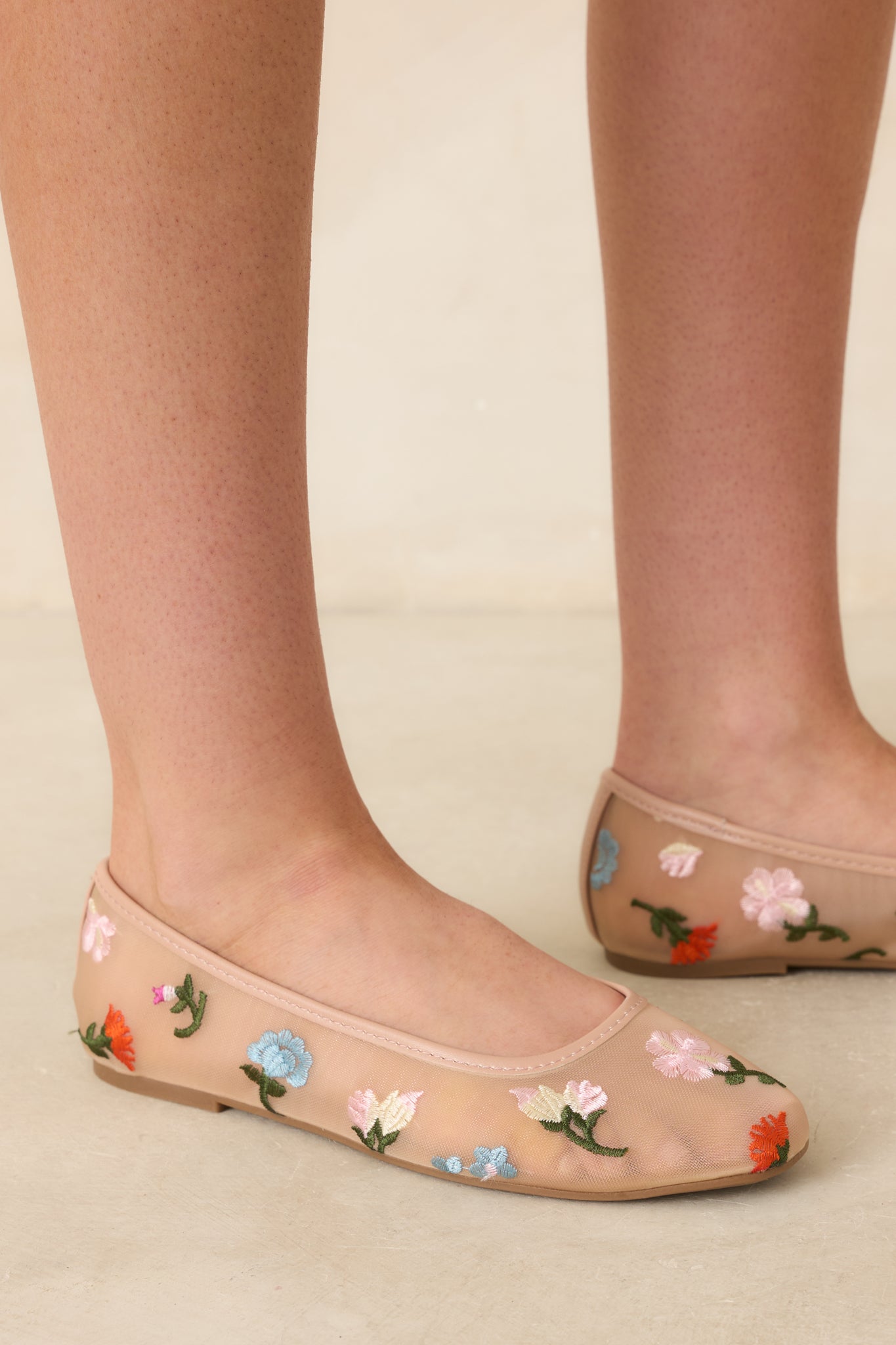 Close cropped angle of nude ballet flats showing breathable mesh fabric and delicate floral stitching