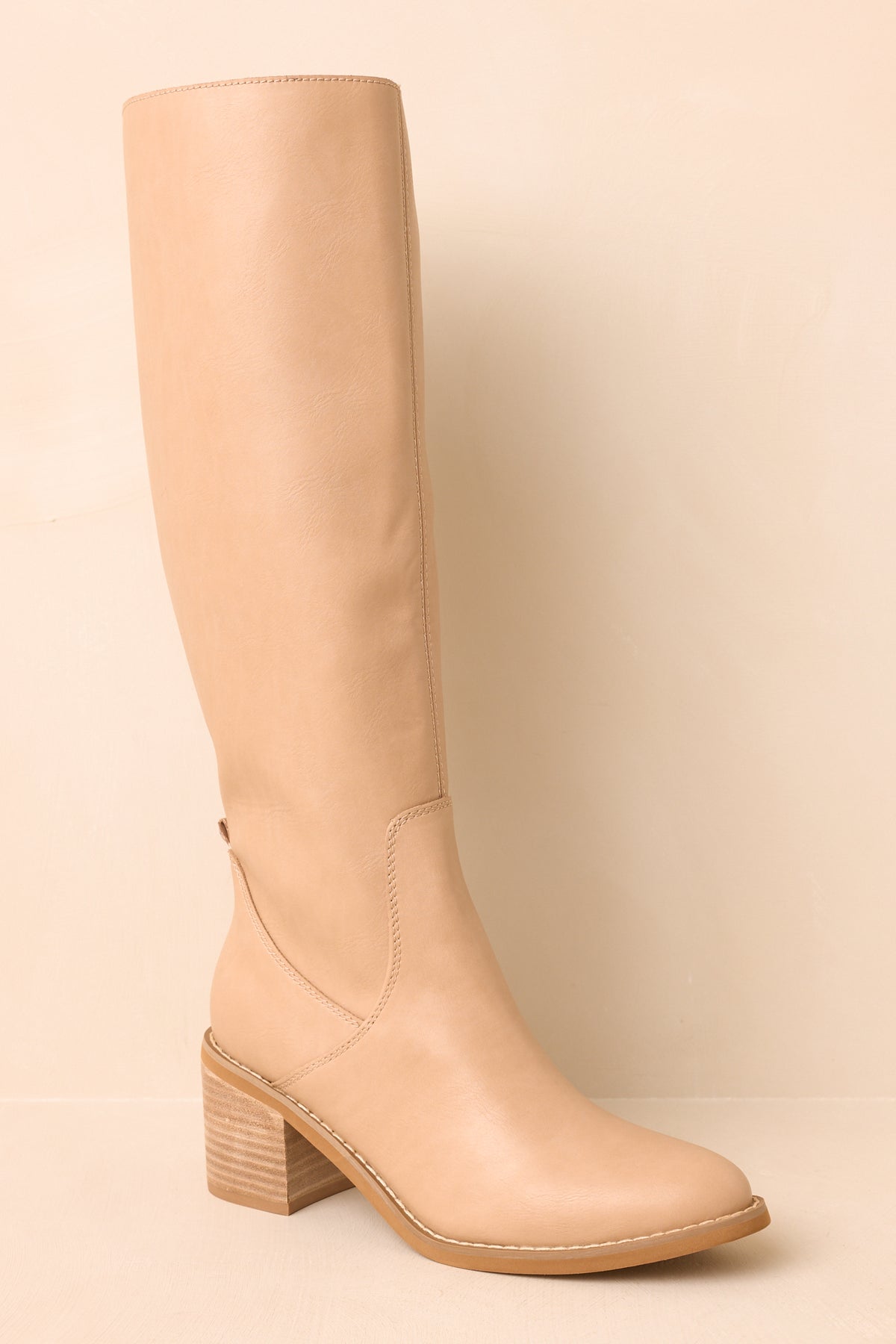 Nude faux leather boots displayed at an angled view, showcasing the almond toe and subtle seam detailing.