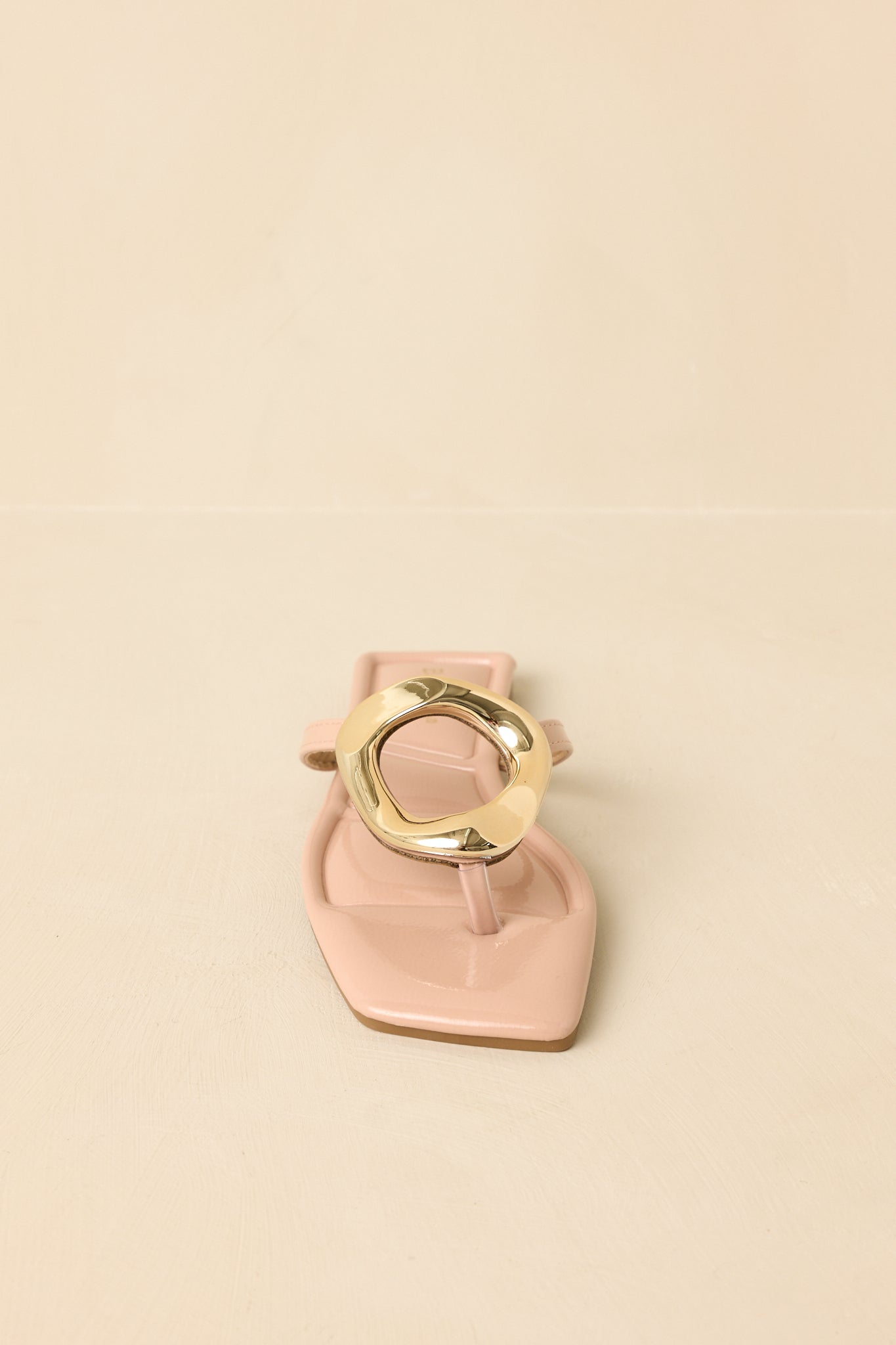 Zoomed-in image of the nude patent sandals emphasizing the gold-tone sculptural ring detail at the vamp.