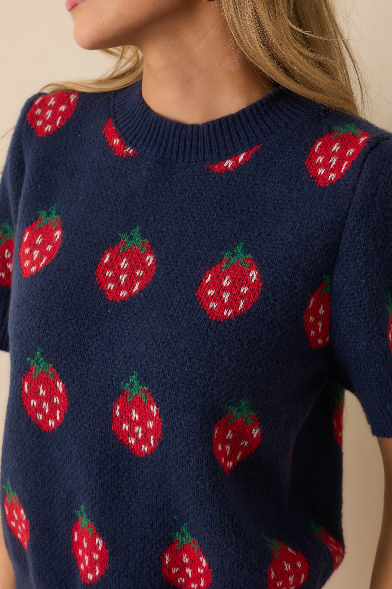 Tight view of red strawberry intarsia on navy knit, showing texture and ribbed trim.