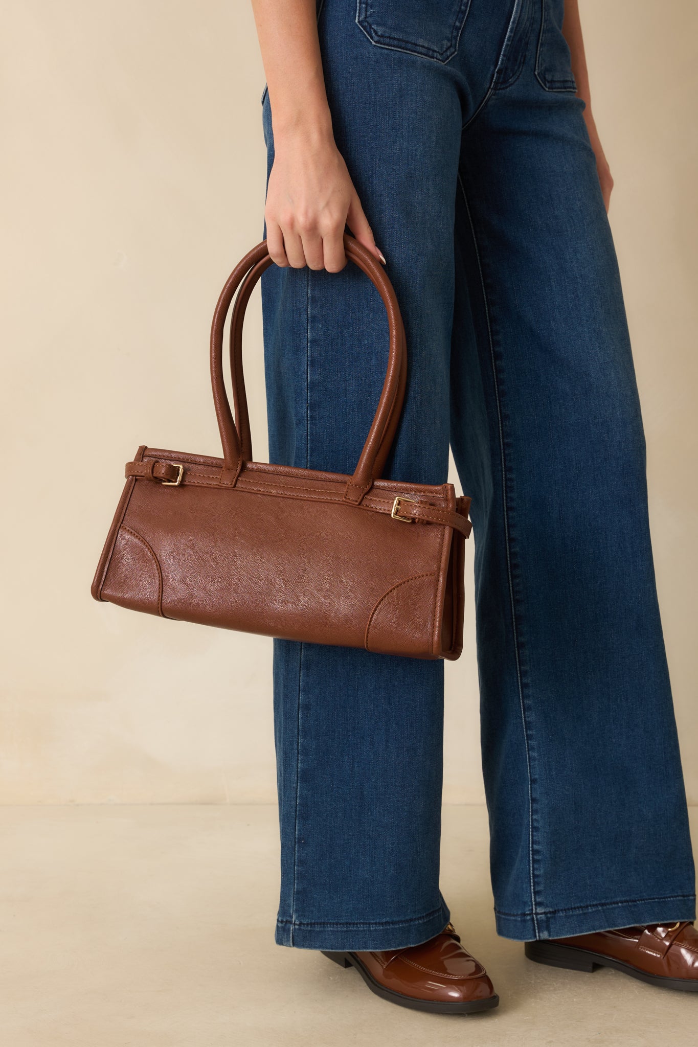Cognac brown faux leather handbag shown with its structured rectangular shape and rolled double handles adding a refined touch.