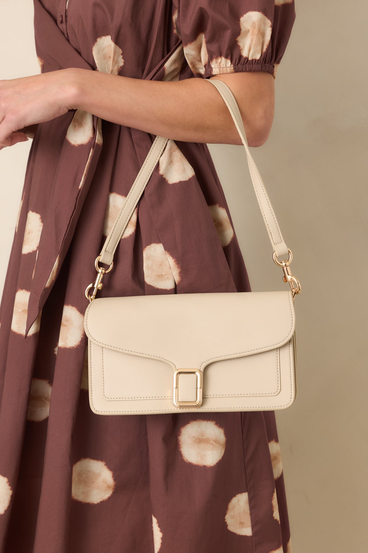 Off-white faux leather handbag with a structured rectangular shape, contoured envelope flap, gold-tone buckle clasp, and detachable strap.