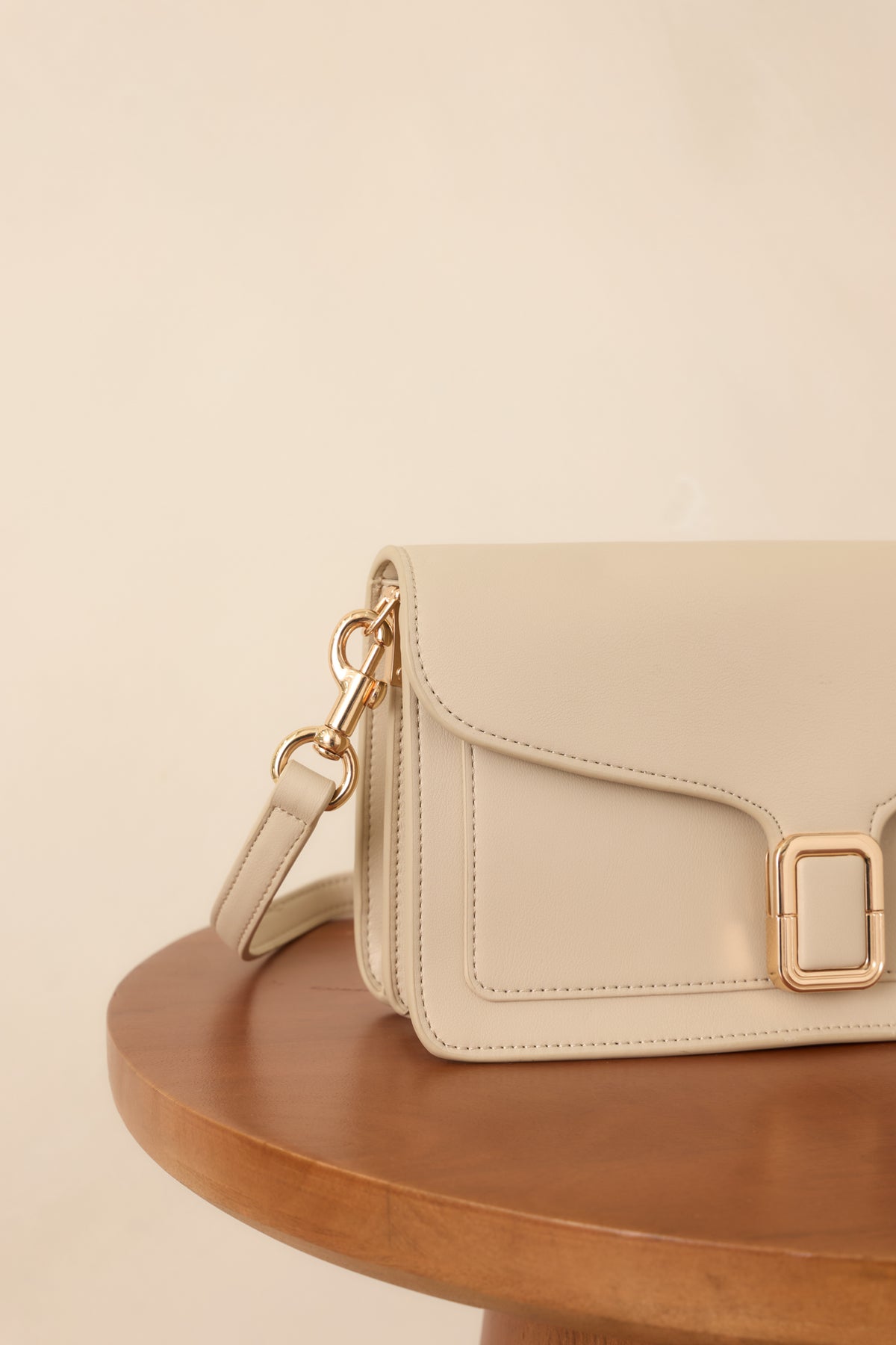 Close-up of the off-white faux leather handbag showing the polished gold-tone buckle clasp and precise tonal edge stitching.