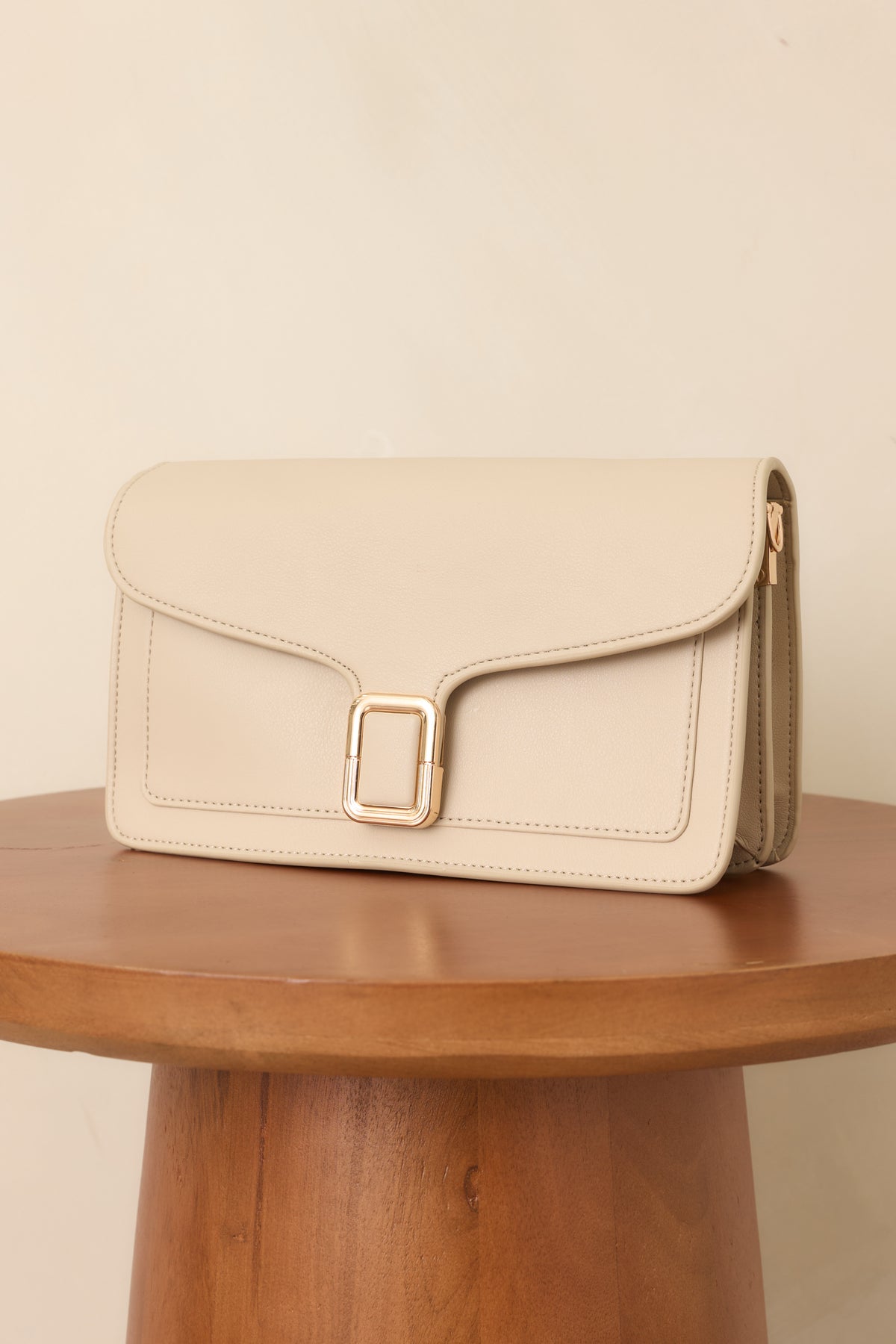 Off-white faux leather handbag highlighting the structured silhouette, envelope flap, gold-tone buckle clasp, and clean tonal stitching.