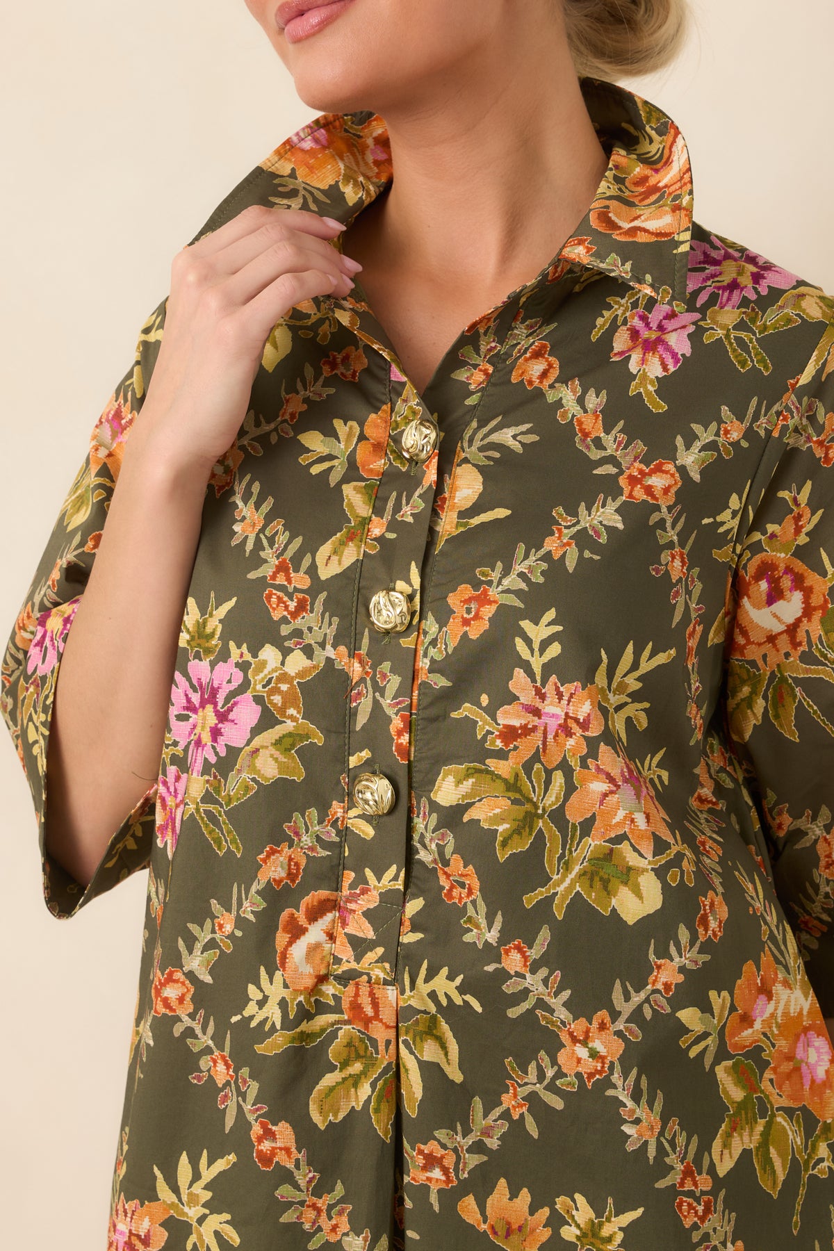 Close-up of the pointed collar, decorative gold-tone buttons, and colorful floral print on the olive dress.
