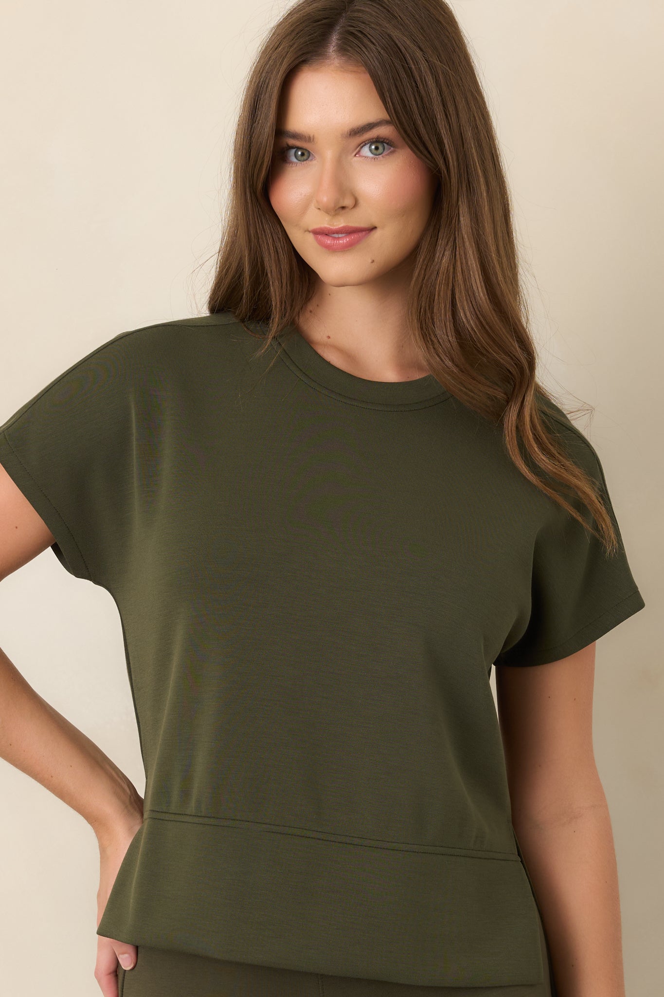 Close view of the olive-green top highlighting the classic crew neckline, smooth spacer fabric, and short sleeves.