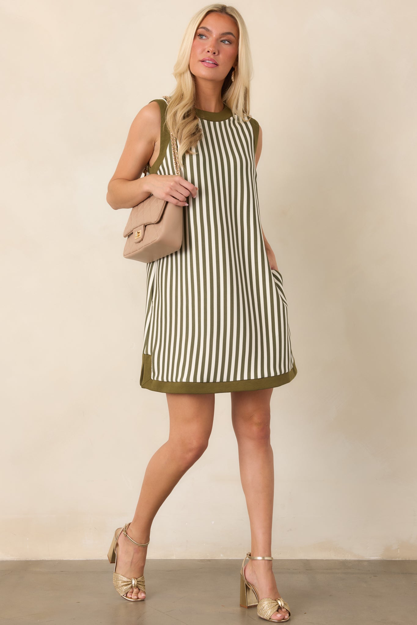 Relaxed straight-fit dress with alternating olive and ivory stripes, contrasting trim around the neckline, and functional side pockets.