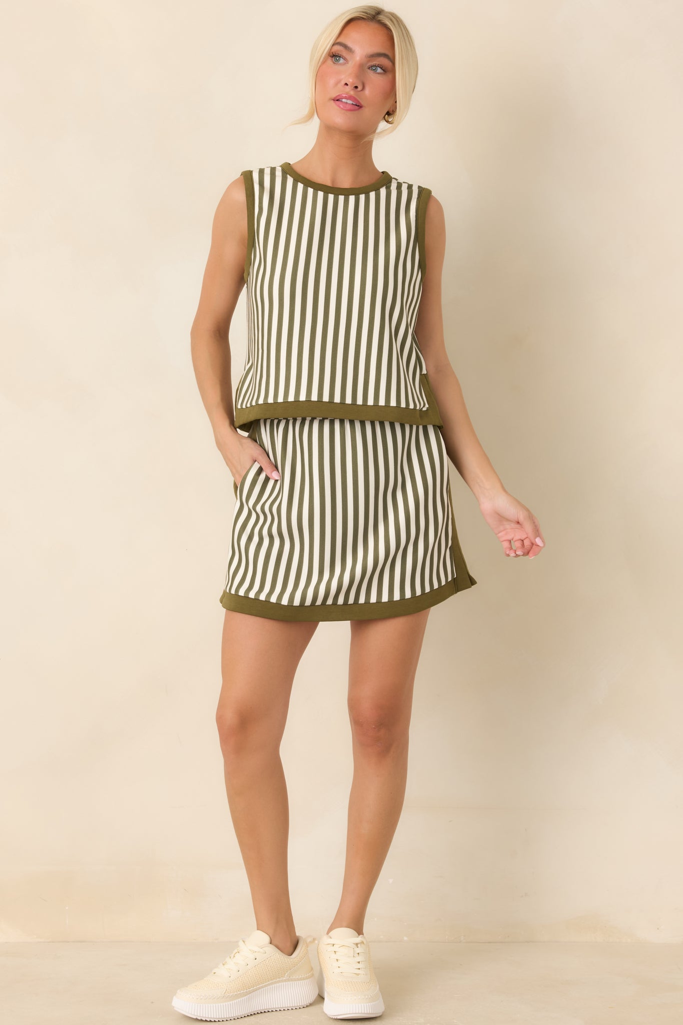 High-rise striped mini skirt featuring alternating olive and ivory vertical lines, practical side pockets, and contrasting olive edging.