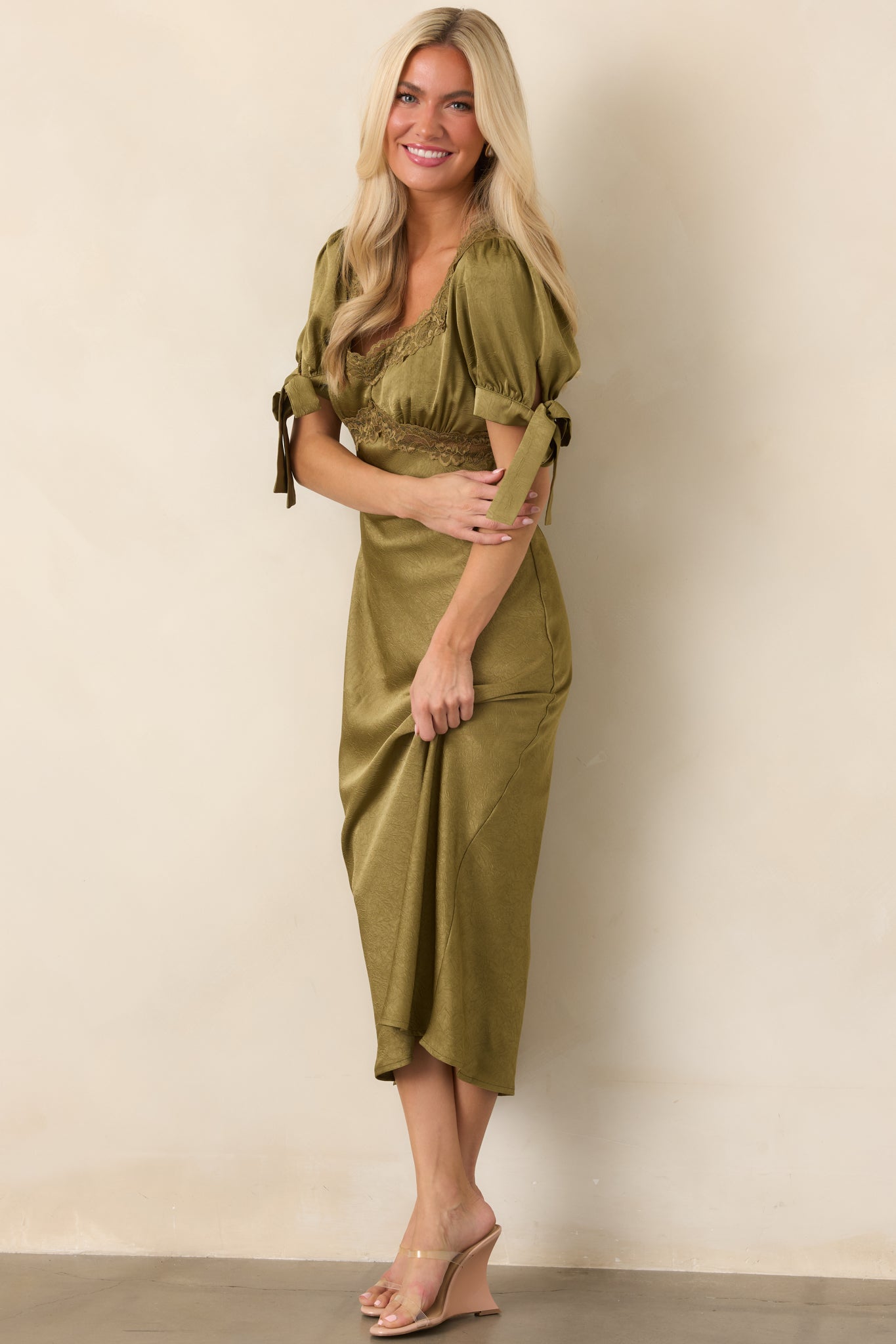 Olive satin midi silhouette featuring an elegant neckline, defined underbust detail, softly gathered sleeves, and a full flowing skirt.