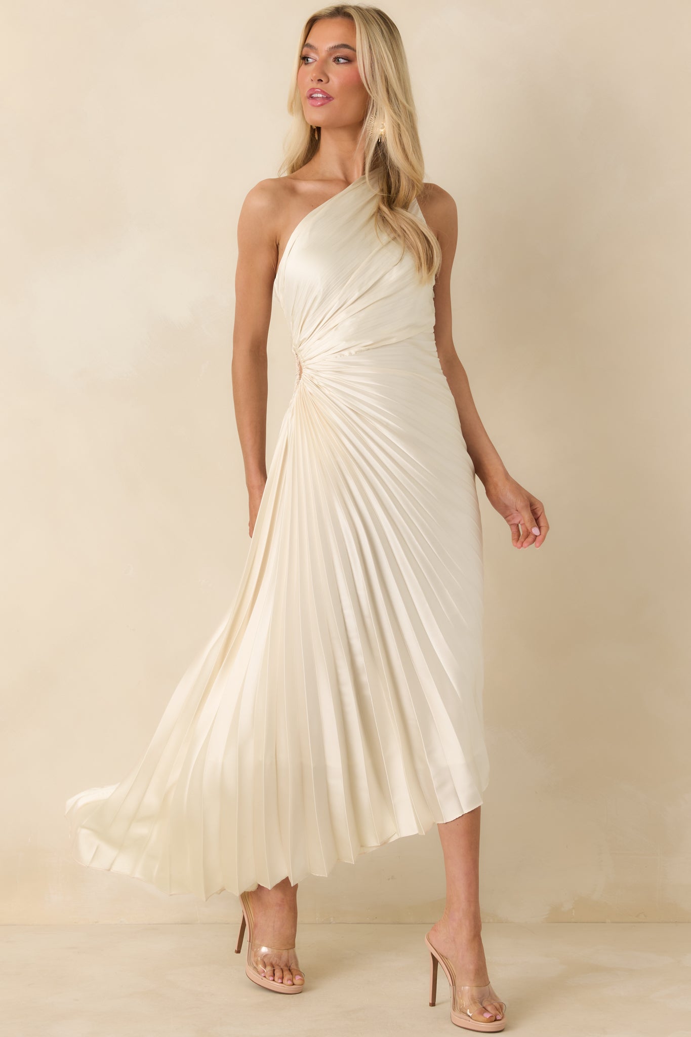 One-shoulder ivory dress featuring allover pleating, a fitted bodice with side cutout, and asymmetric hemline.