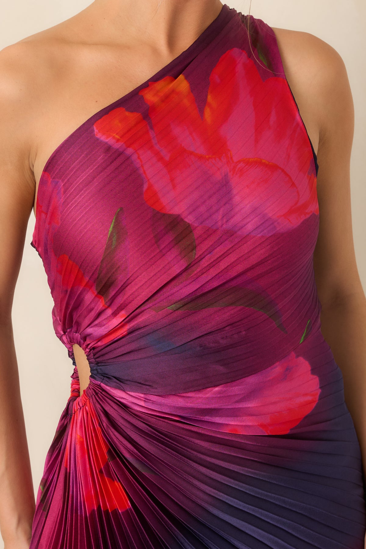 Close-up highlights the one-shoulder neckline, sculpted pleating, waist ruching, and cutout detail against the vibrant floral print.