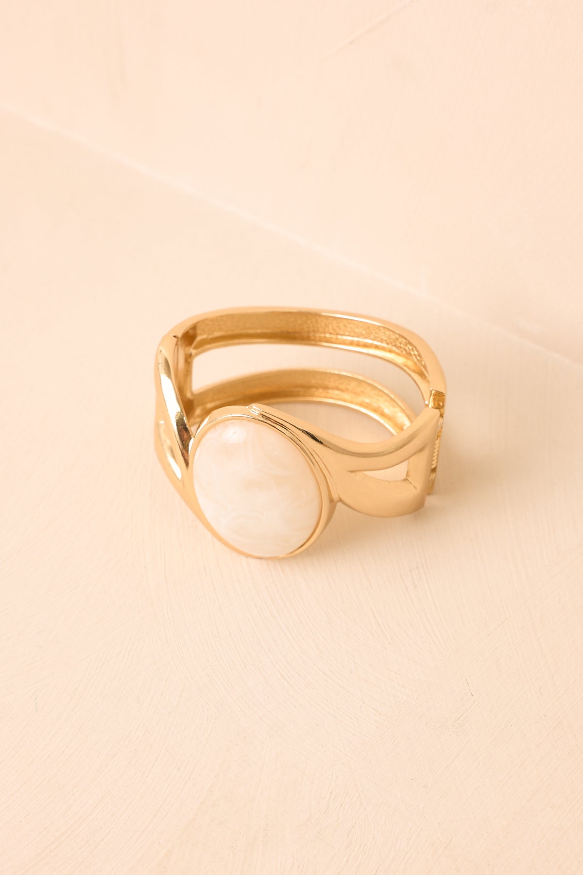 Open cuff bracelet displayed against a beige background, highlighting the ivory cabochon centerpiece and refined geometric construction.
