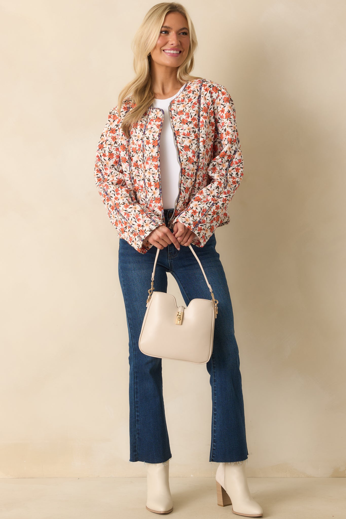 Quilted jacket with orange multicolor floral print, round neckline, and vertical seam paneling.