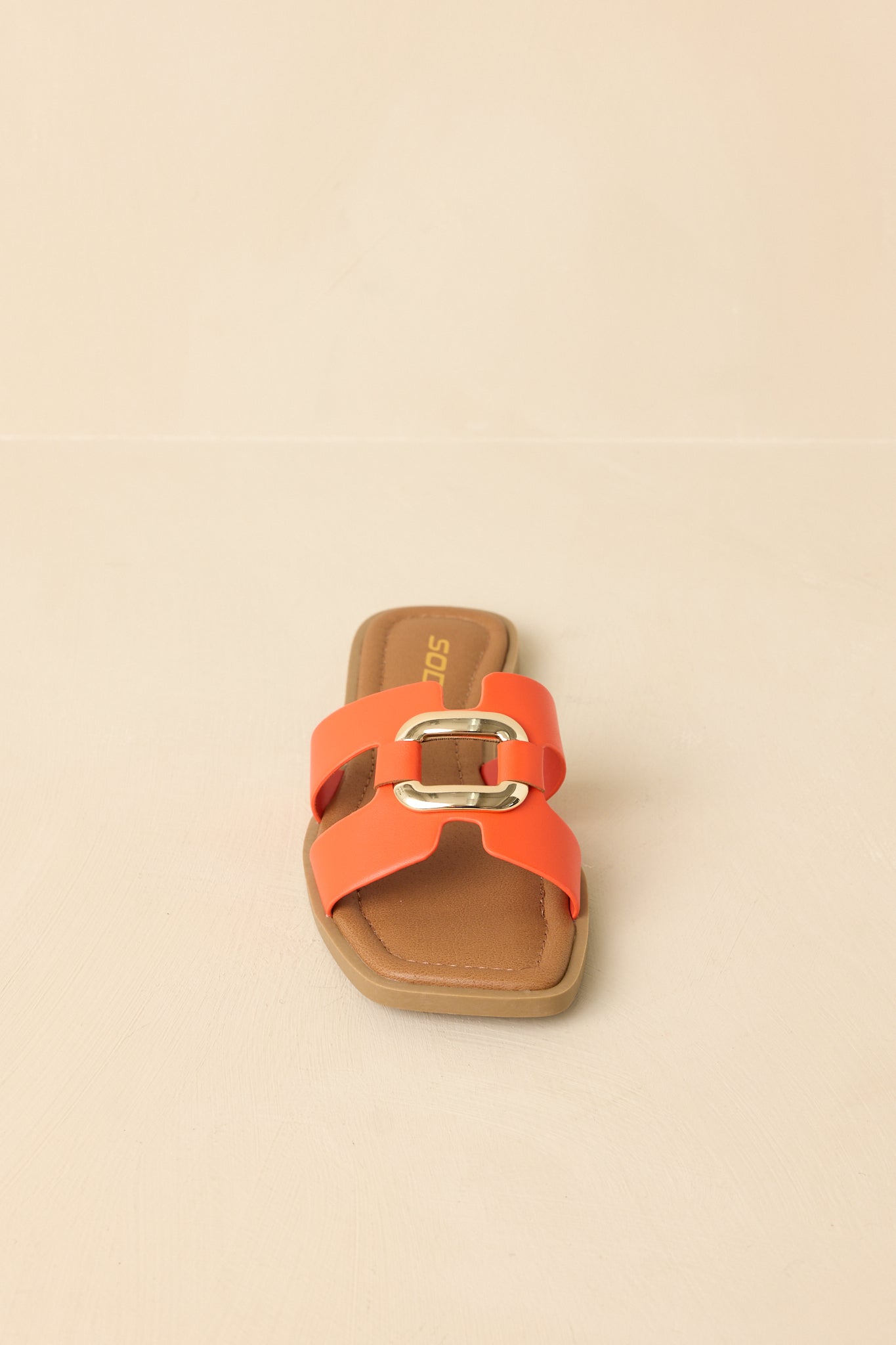 Full view of orange flat slide sandals against a beige background showing the open square toe and wide strap design.