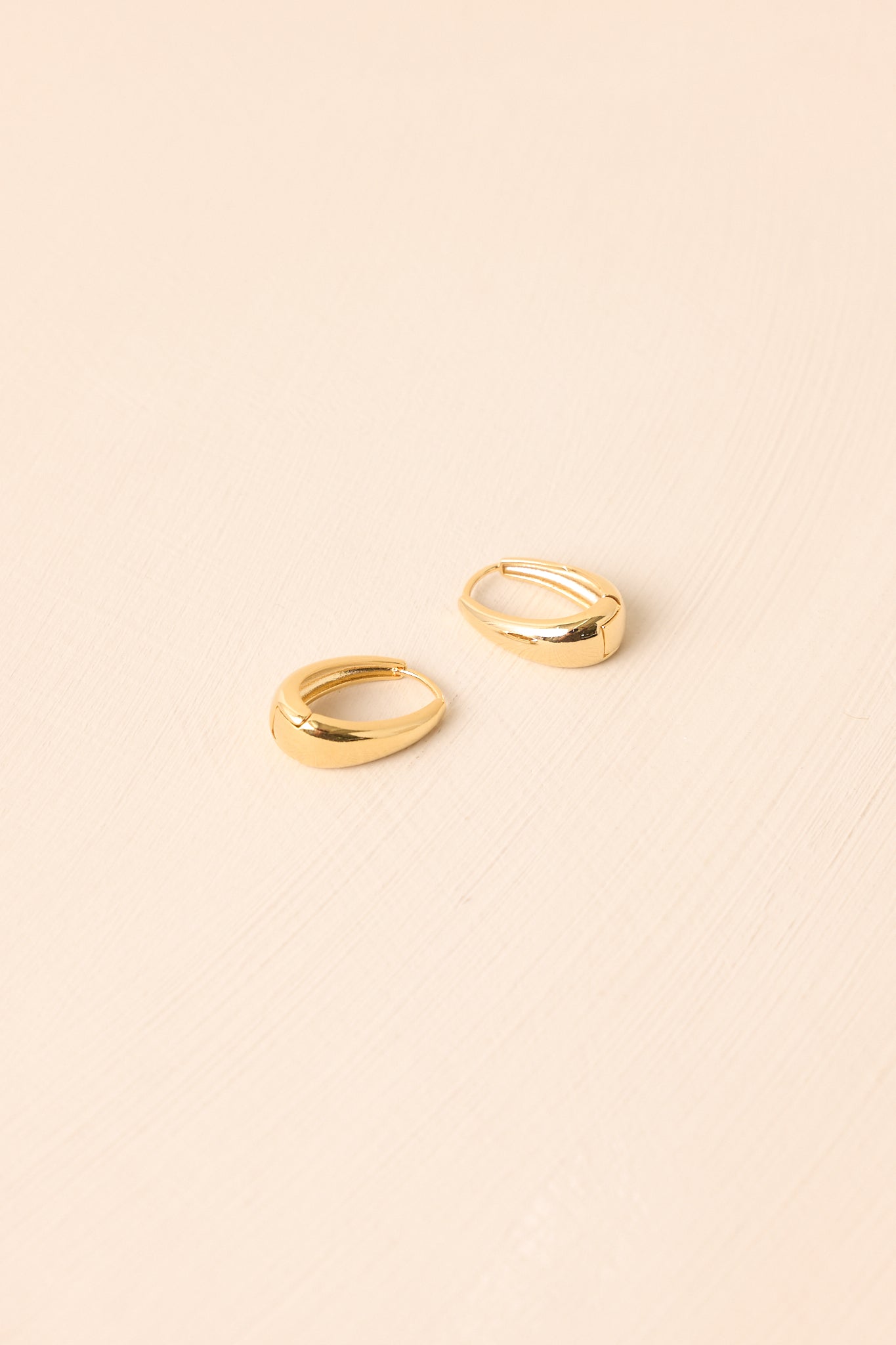 Tapered oval earrings displayed on a beige background, emphasizing their sleek shape and glossy finish.