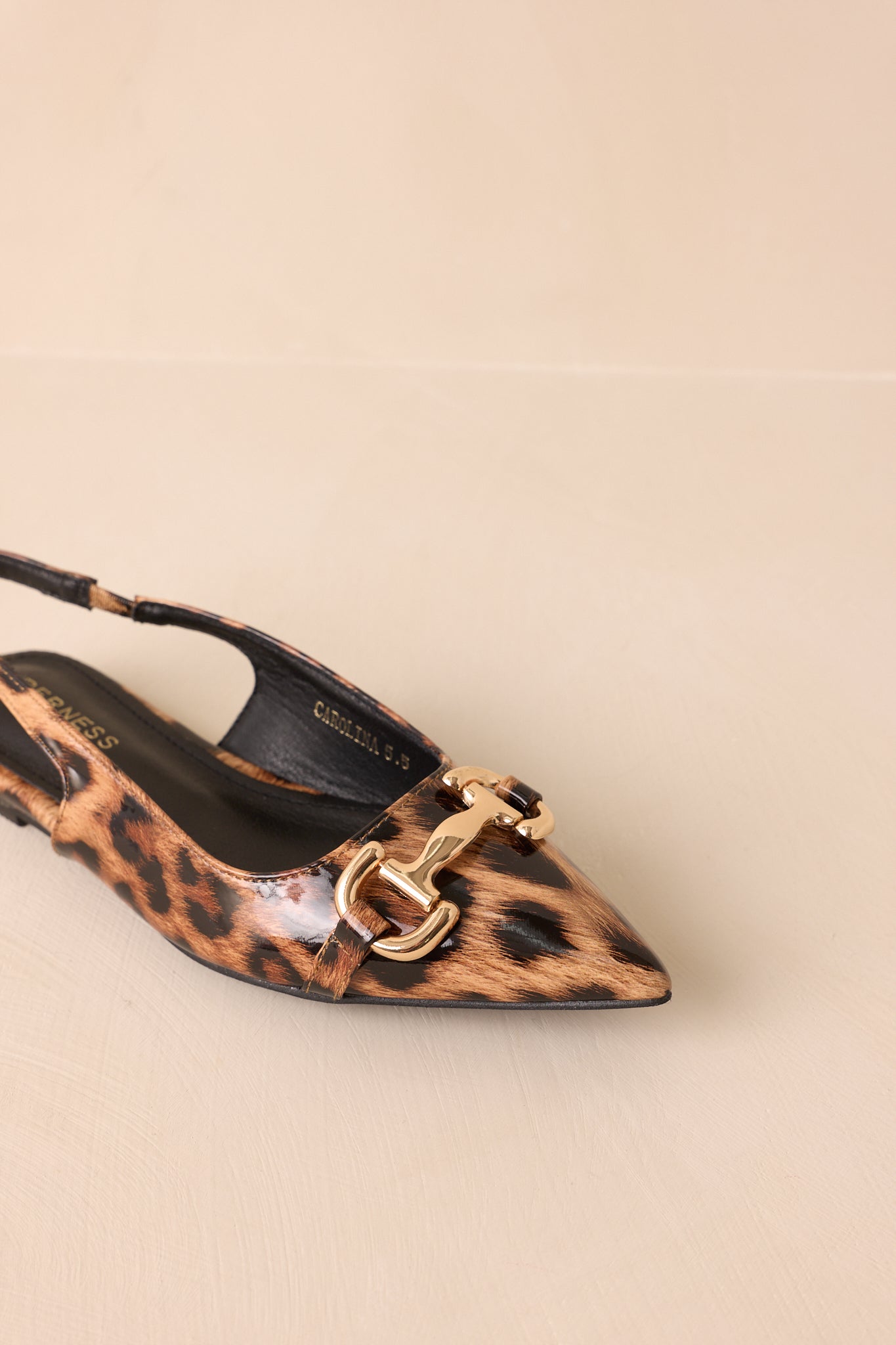 An overhead angled view of the flats on a beige background, focusing on the pointed toe and smooth patent surface.