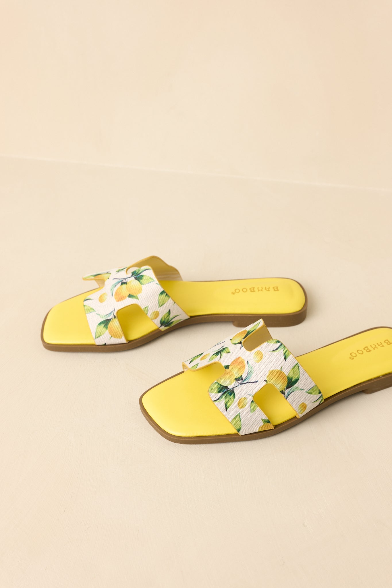 Overhead view of fruit print slide sandals on beige background featuring open toe and bold strap design