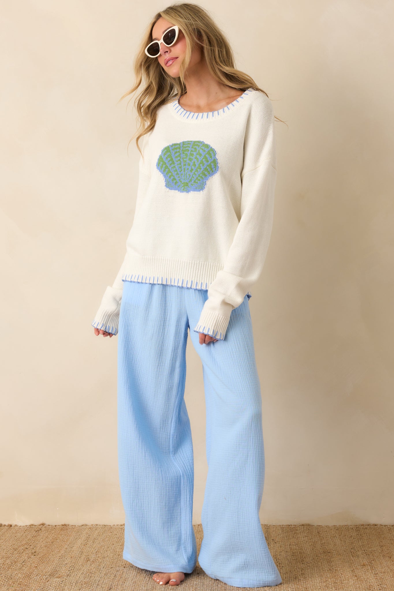 White sweater with soft knit fabric, relaxed fit, and subtle textured shell graphic on the chest.