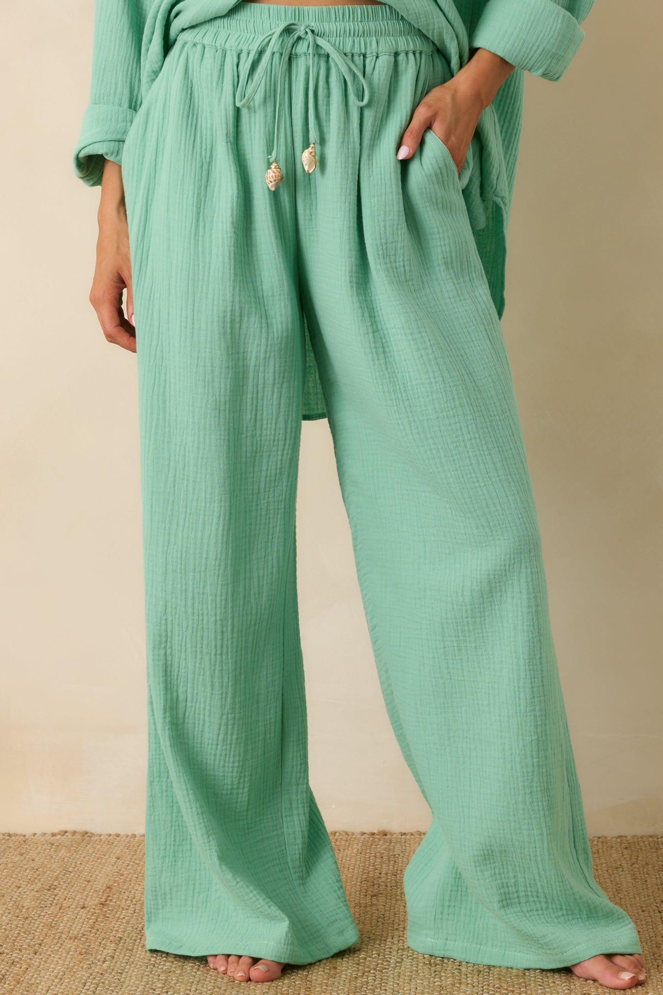 Close front crop of seafoam green cotton pants highlighting elastic waistband and decorative tassel ties.