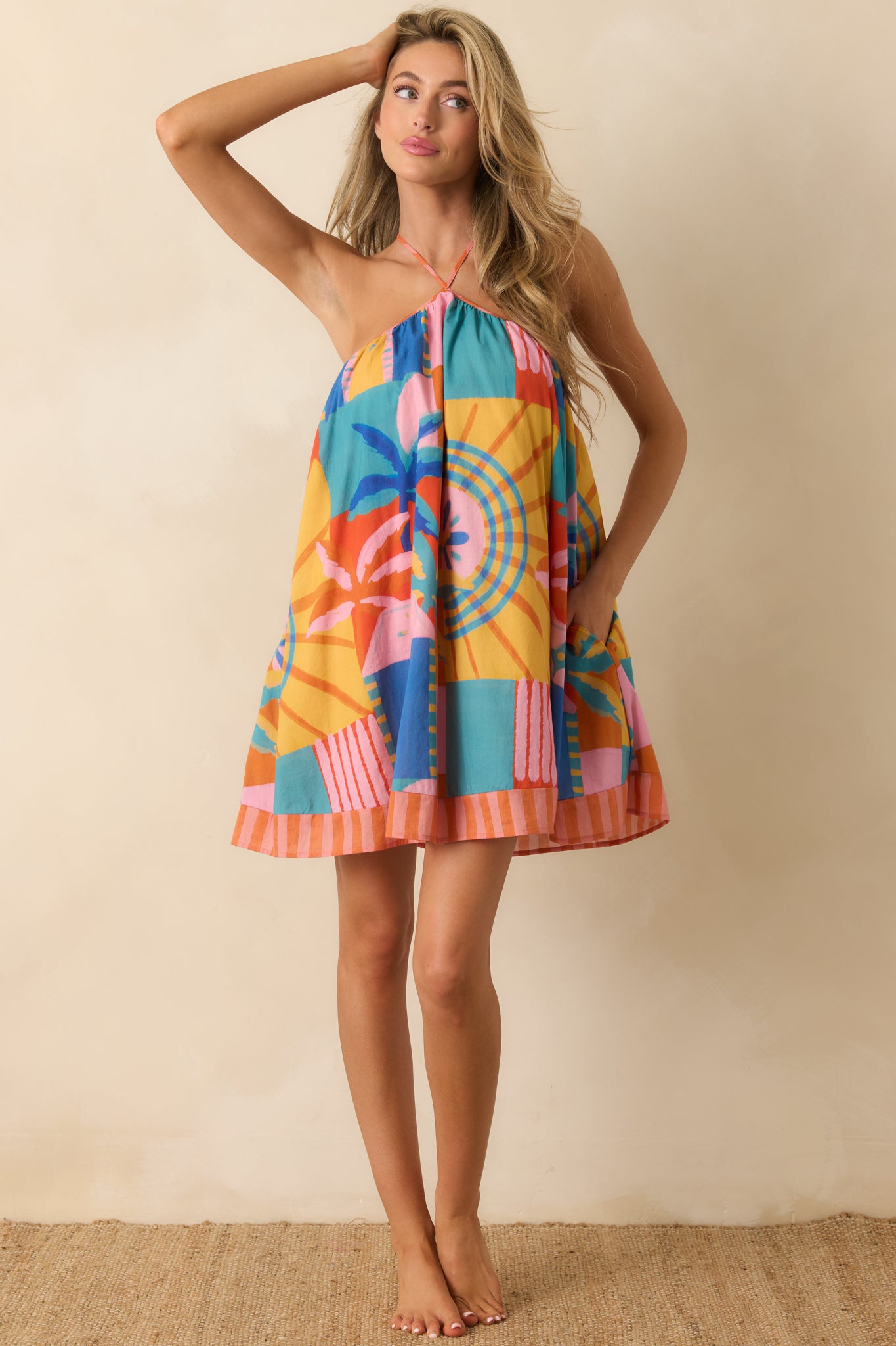 Tropical mosaic mini dress with adjustable crisscross straps, a breezy silhouette, and striped trim detail along the hemline.