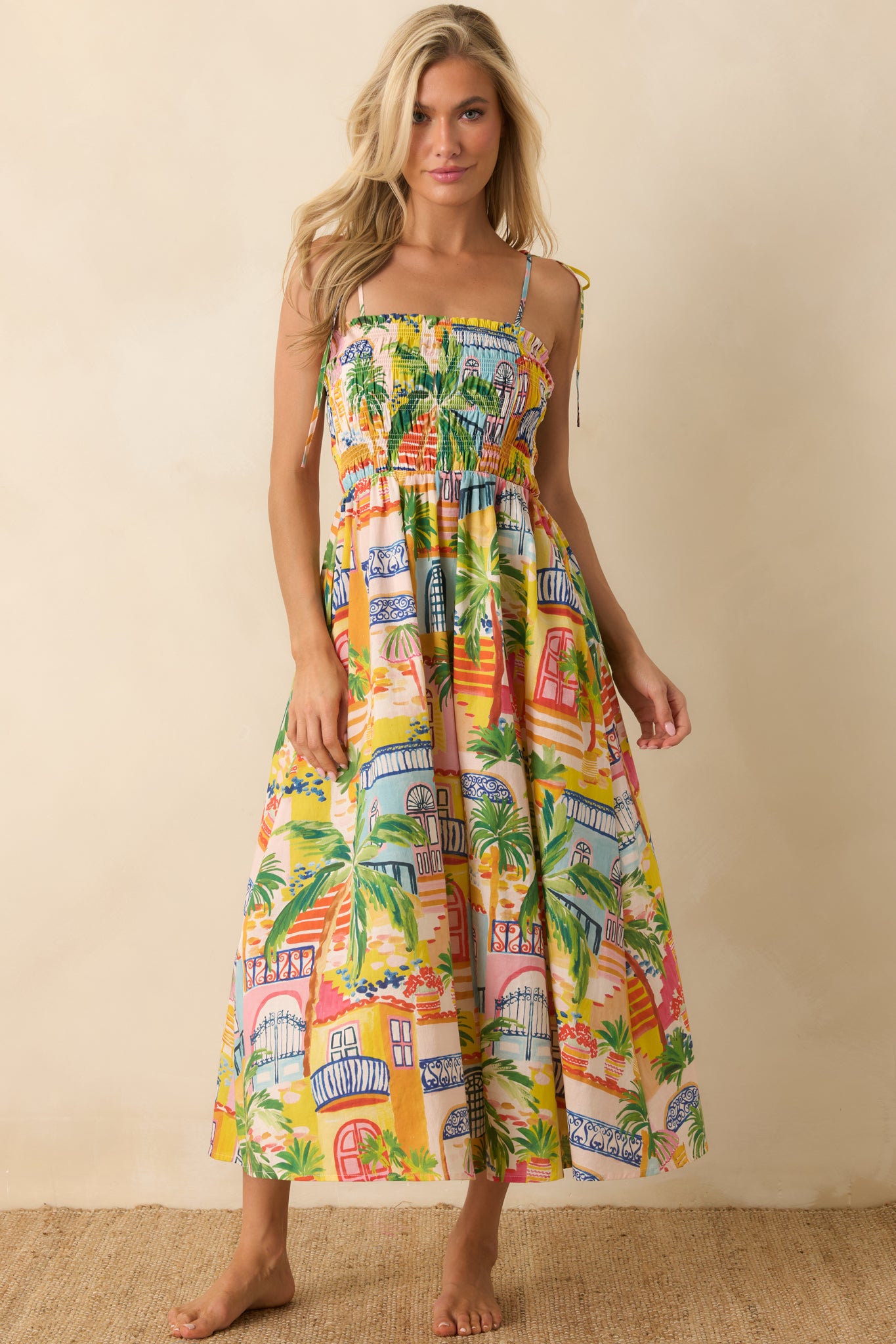 Coastal-inspired cotton midi dress featuring detailed village artwork, shoulder tie straps, and a relaxed flowing shape.