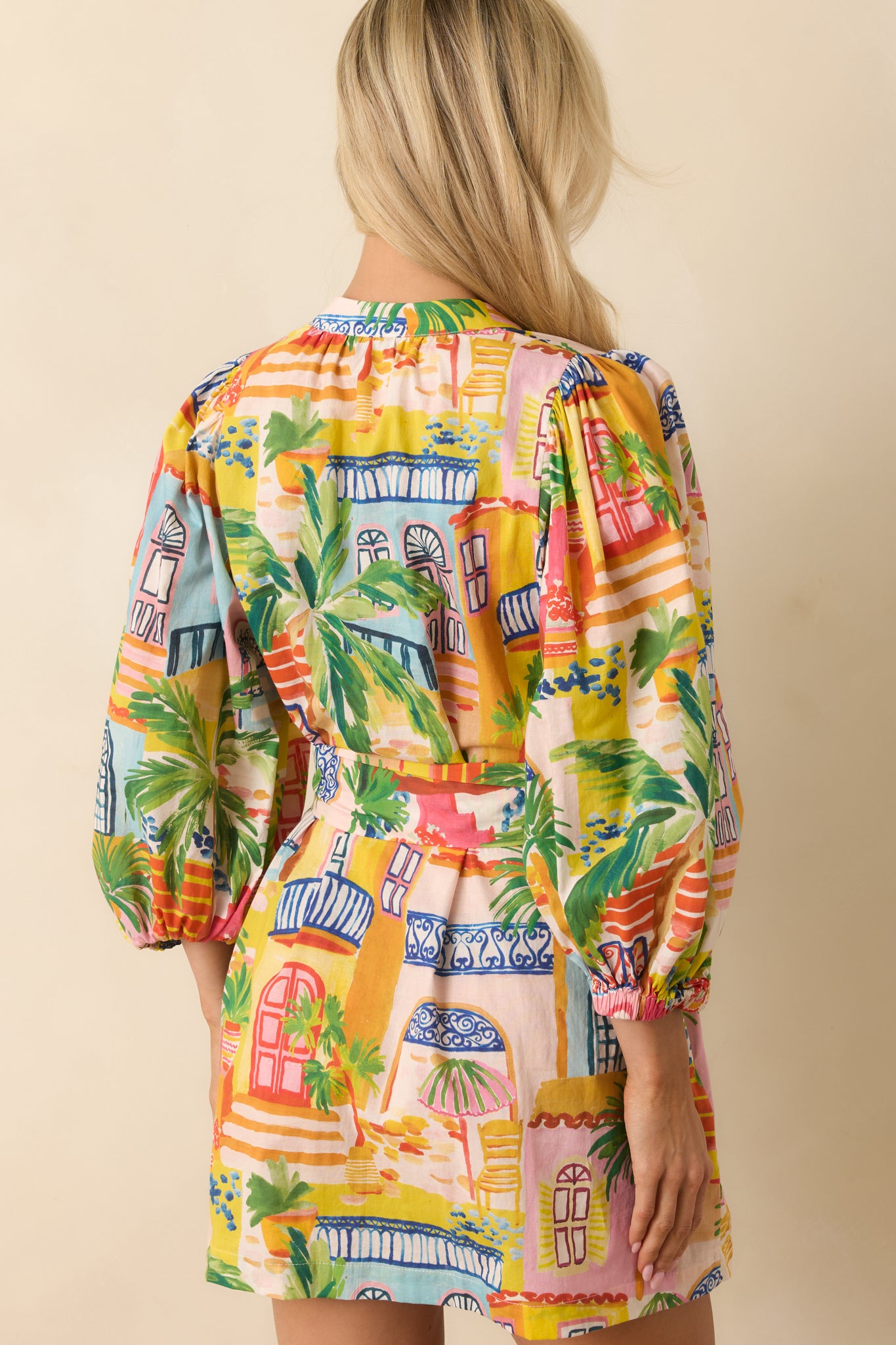 Rear view of the multi-color coastal village print mini dress featuring a relaxed fit, three-quarter puff sleeves, and removable self-tie belt.