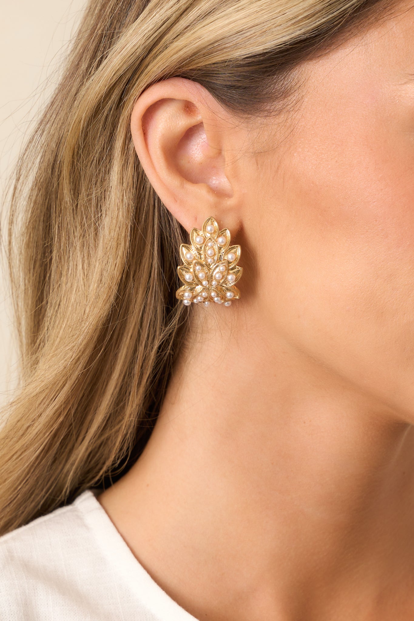 A pair of gold and ivory earrings featuring gold hardware and a j-shaped hoop design, accented with a pile of gold leaf elements and small faux ivory pearls.