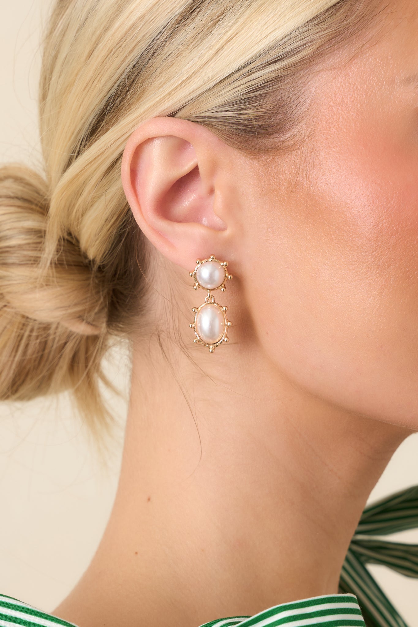 Close-up of pearl drop earrings showing detailed textured gold frames and double-drop design with polished pearls.