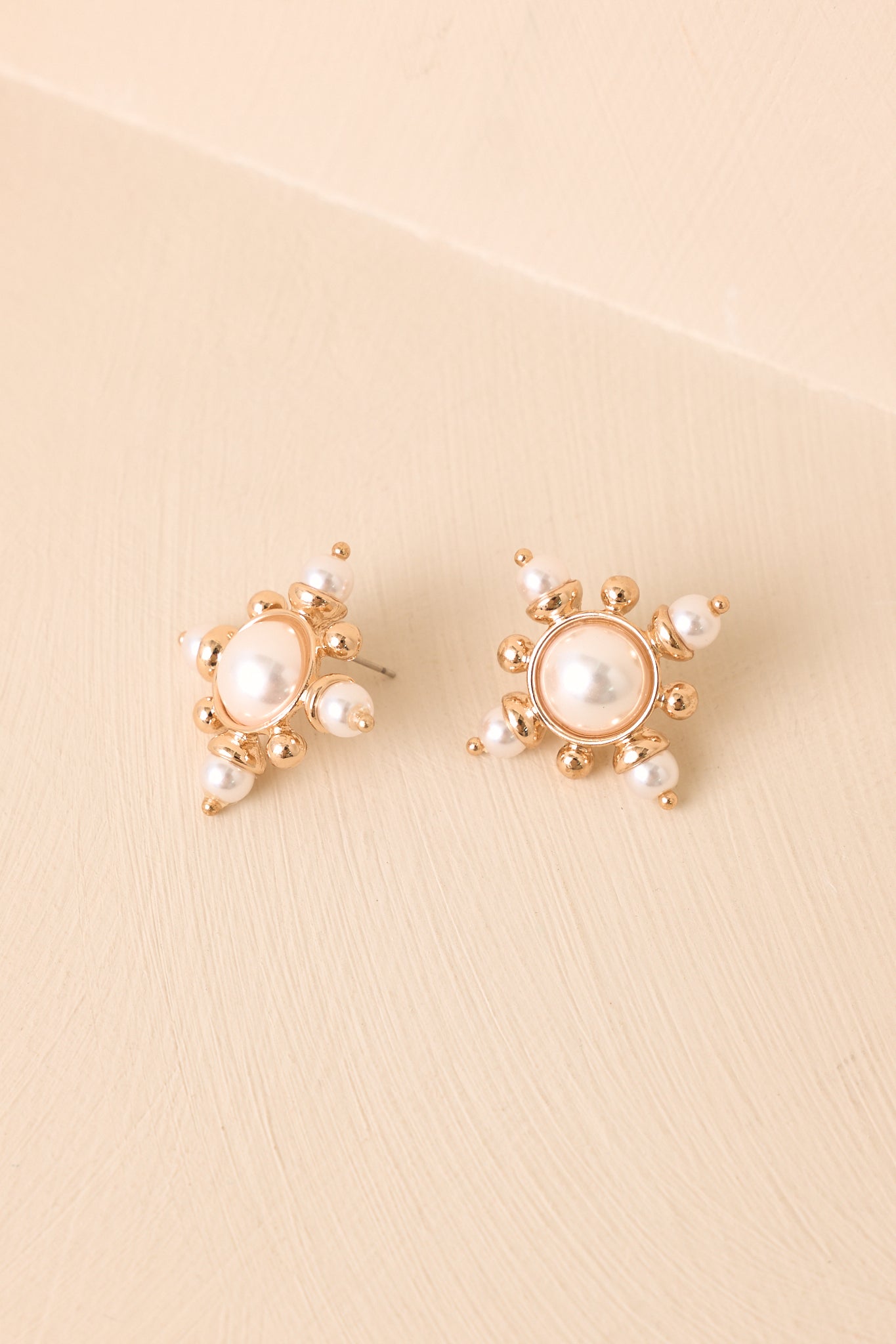 Pearl starburst earrings displayed against a beige background with gold-tone accents and elegant pearl details