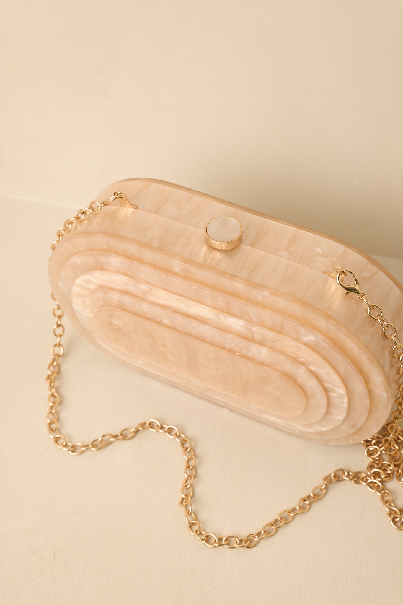 Pearlescent clutch featuring a sculptural oval silhouette, polished hardware, and versatile chain strap.