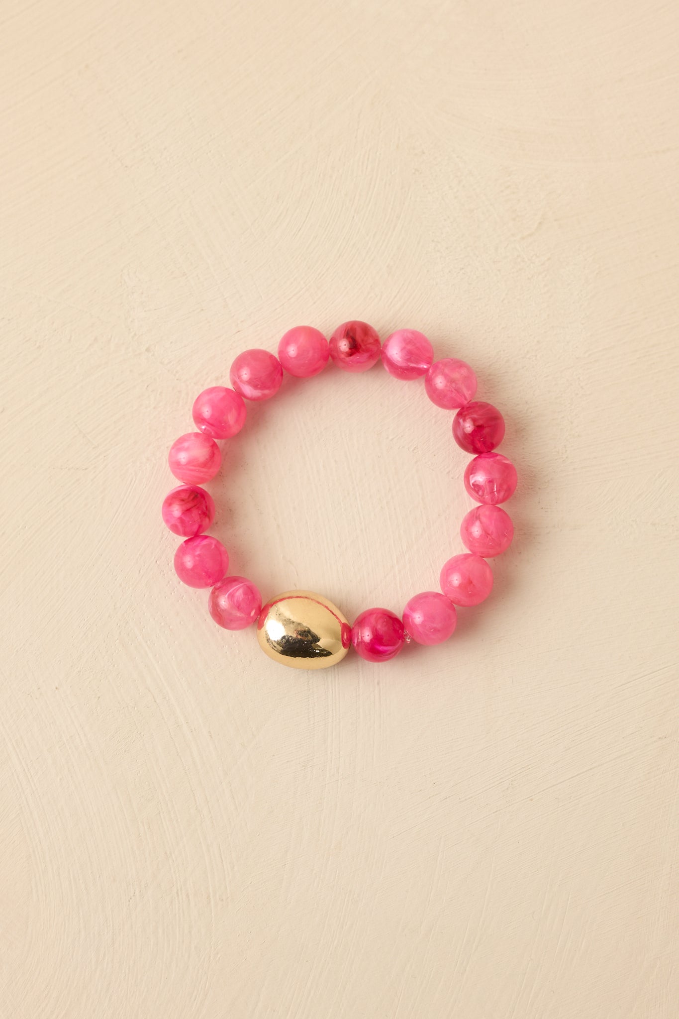 Pink beaded bracelet displayed against a beige background featuring smooth beads and a polished gold-tone detail.