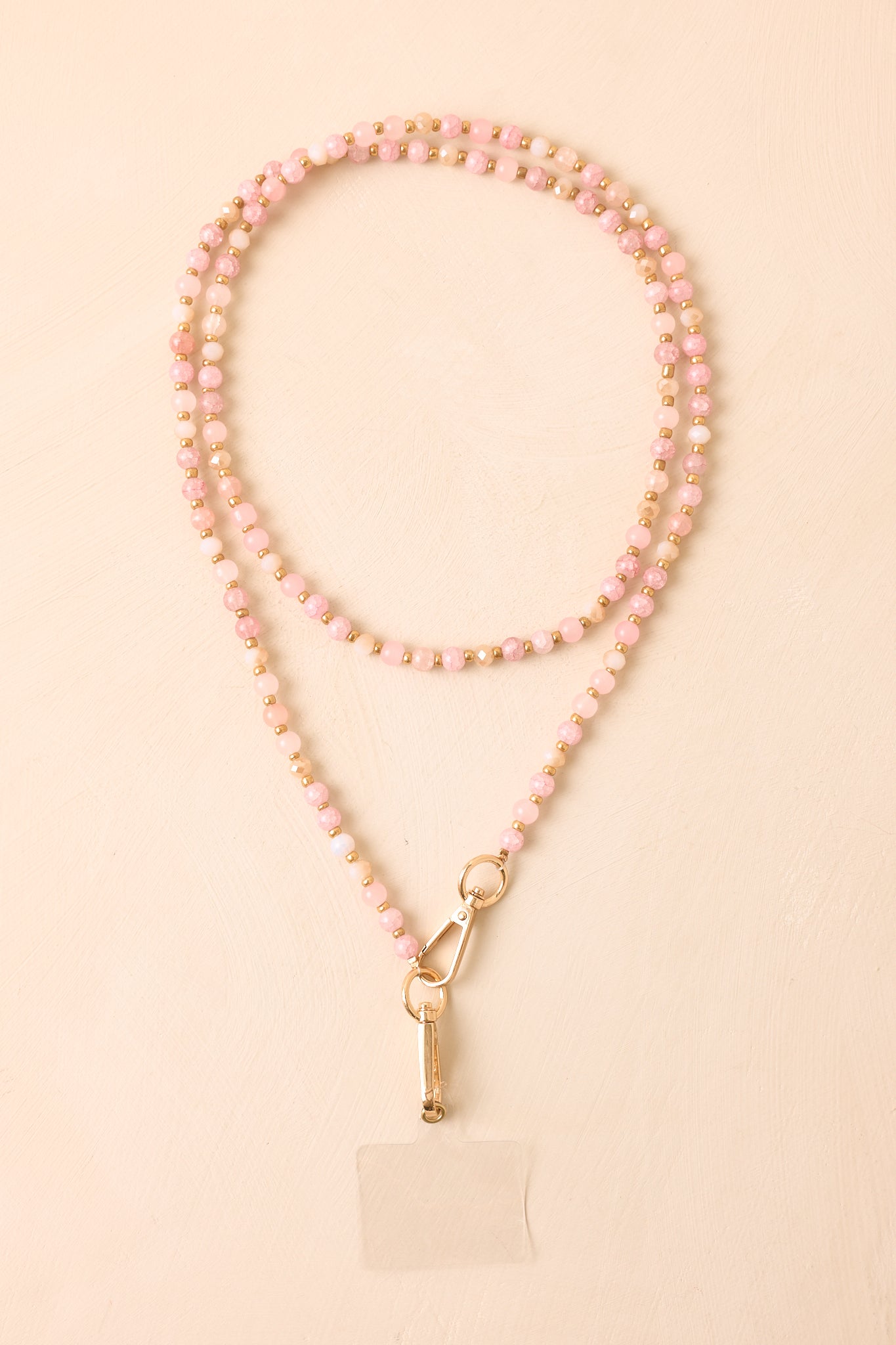 Pink beaded phone lanyard displayed against a beige background, highlighting the polished beads and jewelry-inspired design.