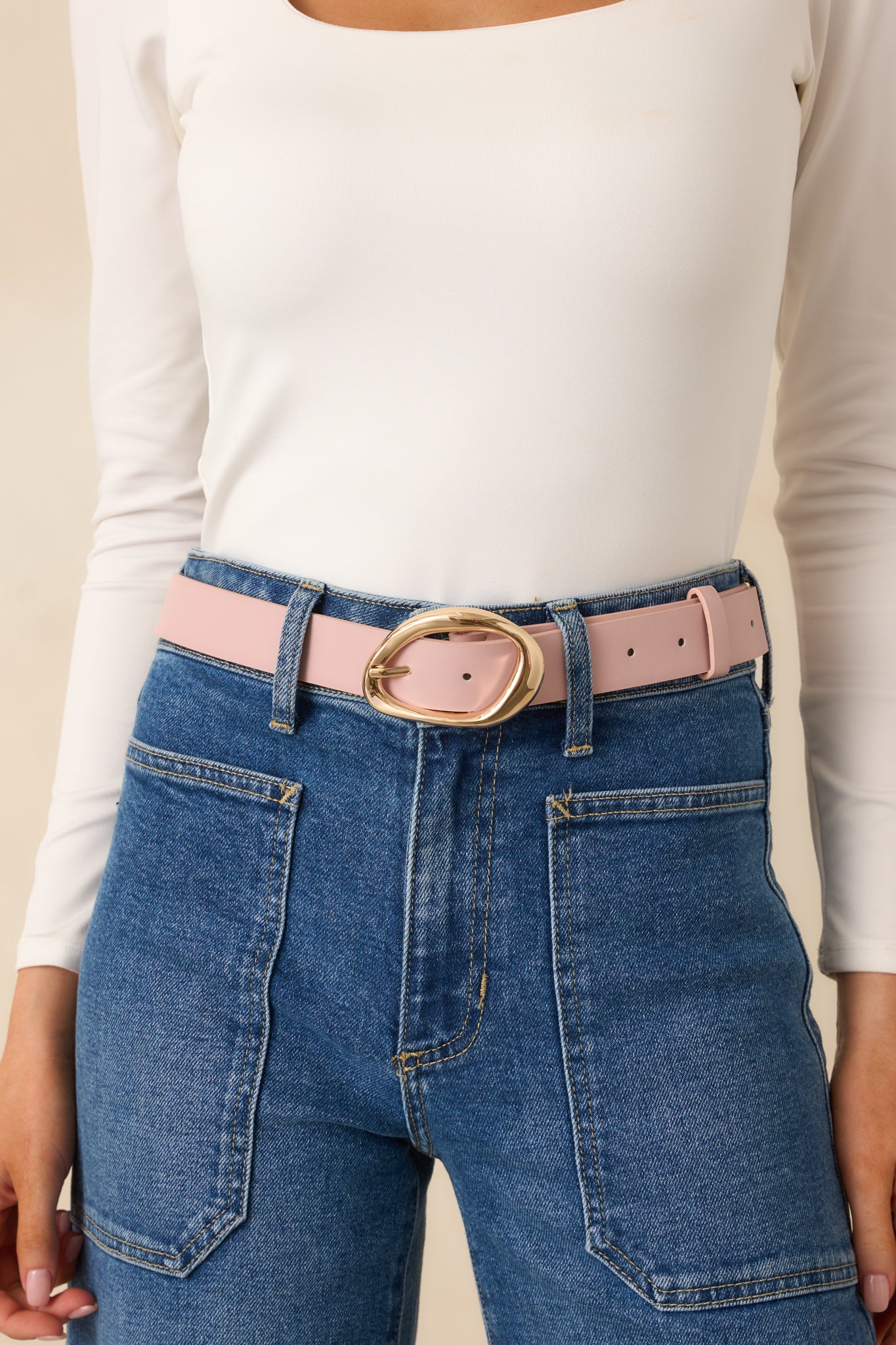 Cropped view of the pink faux leather belt highlighting the abstract oval gold-tone buckle.