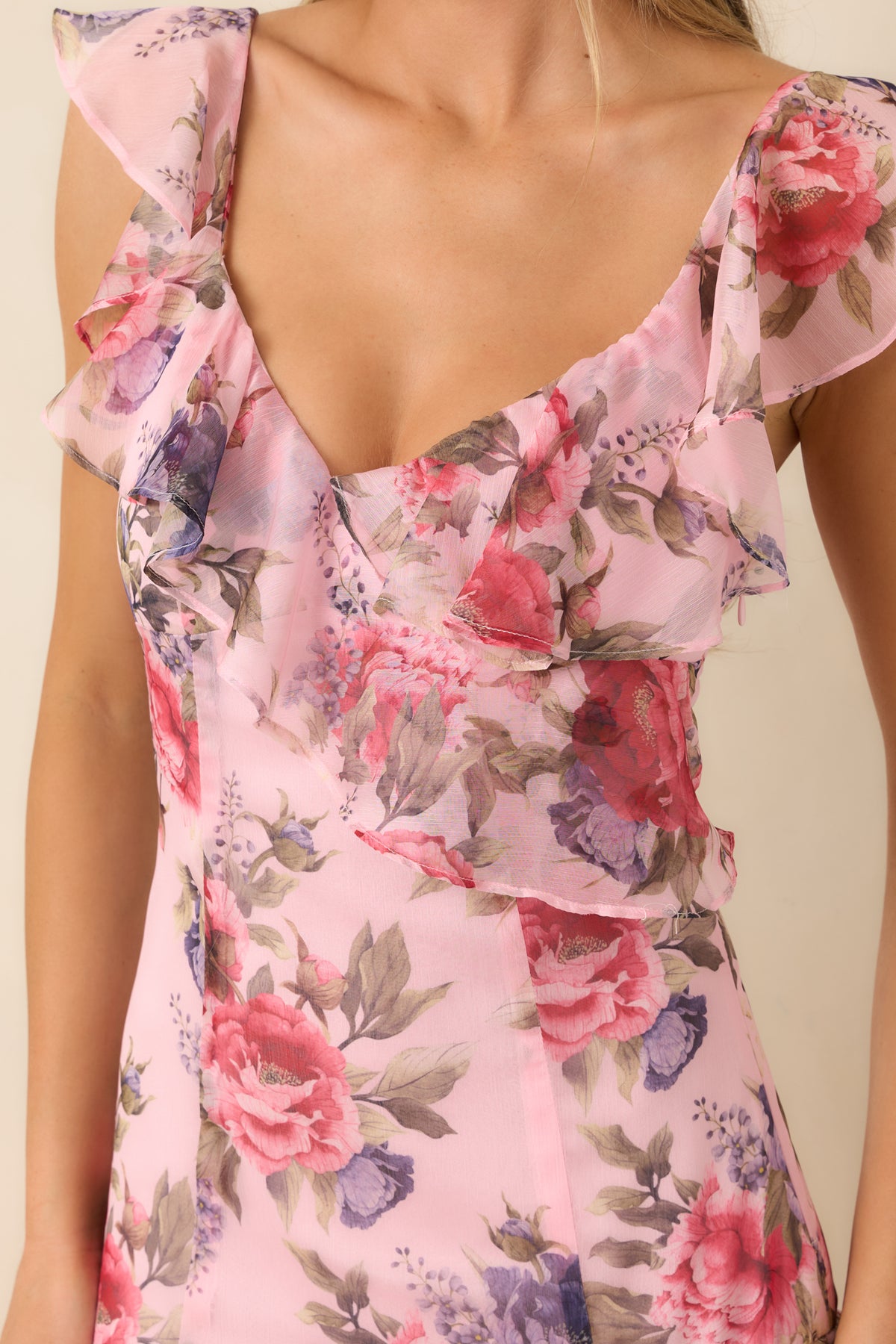 Close-up of the pink floral dress’s V-neckline and fluttering ruffles, showcasing rose and purple blooms among muted green foliage.