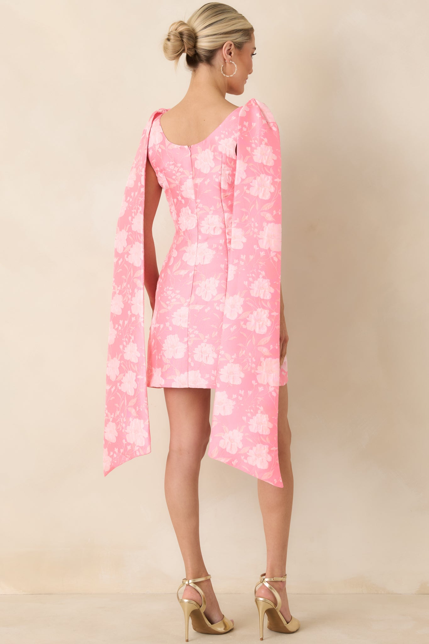 Pink mini dress displaying the sculpted back with wide straps tied into a voluminous bow and smooth jacquard fabric.