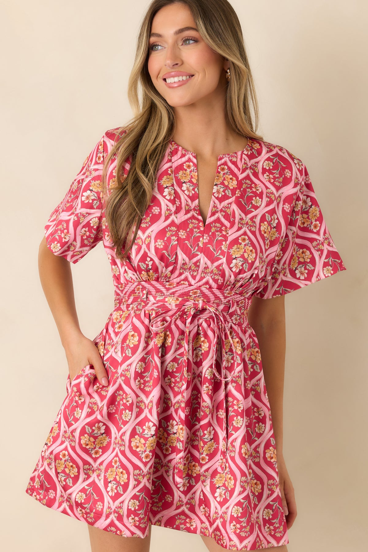 Pink mini dress highlighting the split neckline and colorful floral bouquets against a trellis background.