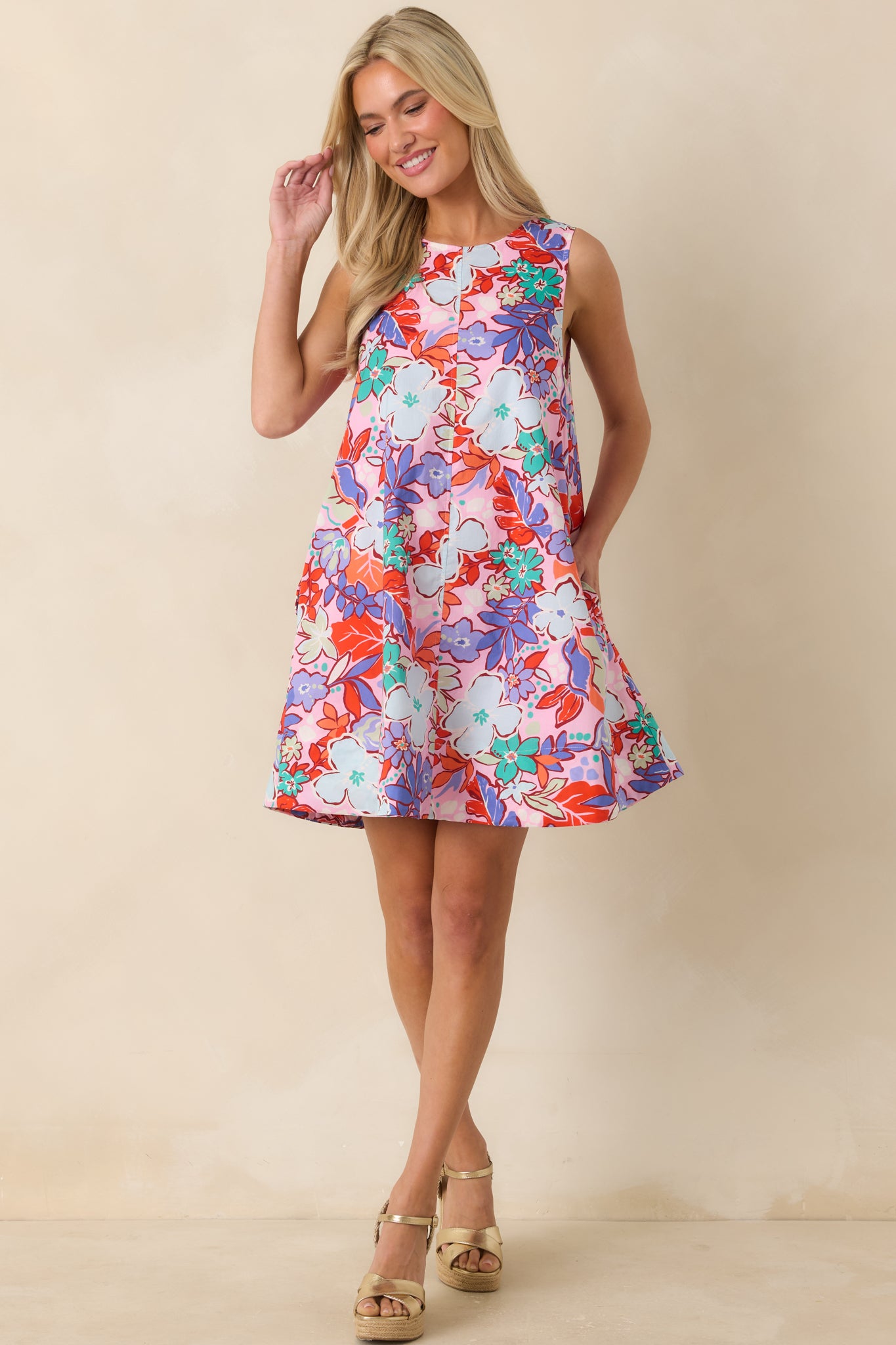 Pink multi floral mini dress featuring a sleeveless silhouette, round neckline, relaxed swing shape, hidden side pockets, and vibrant allover floral pattern.