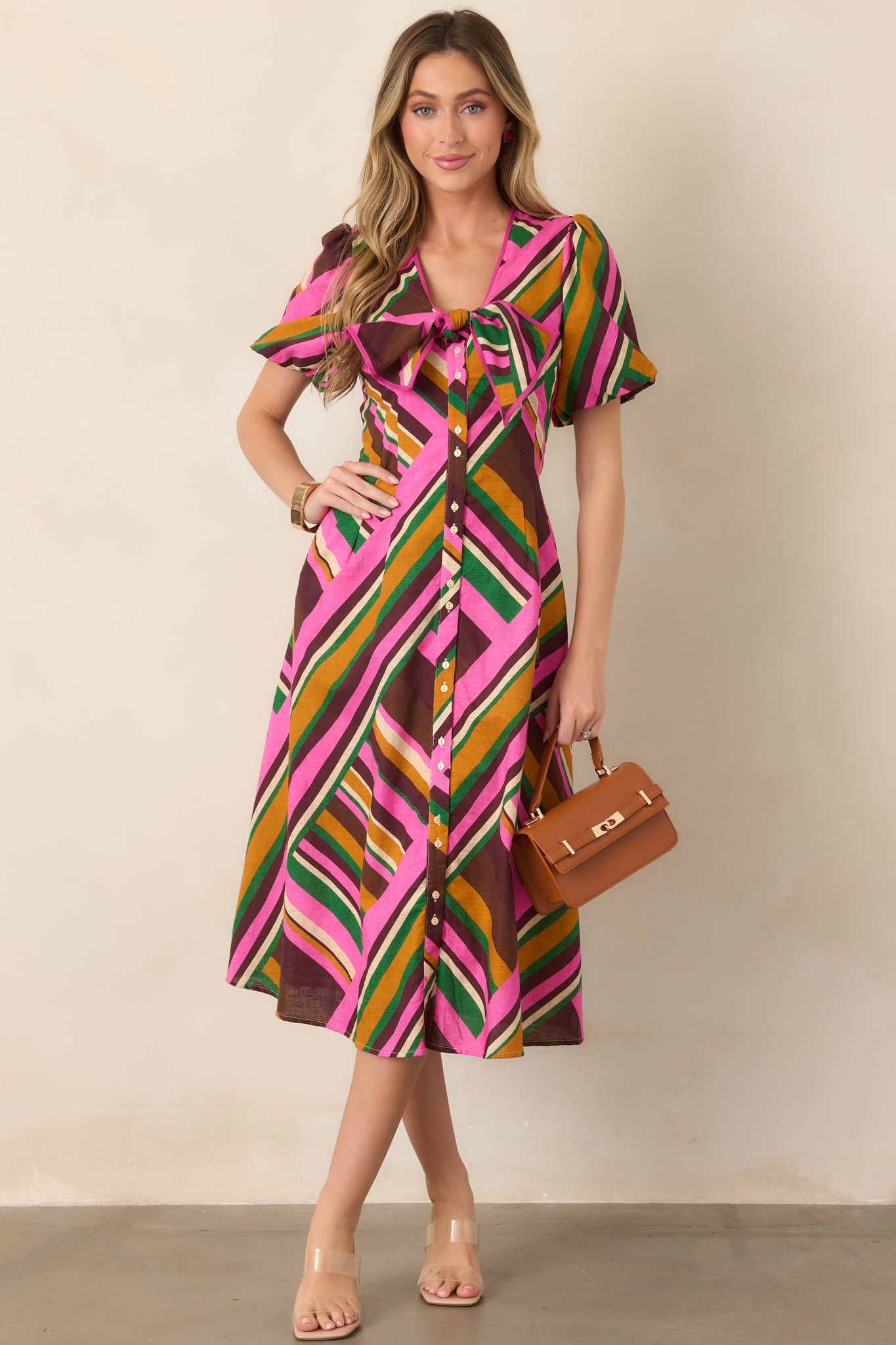 Pink multi geometric stripe midi dress with puff sleeves, a deep V-neckline, statement bust tie, smocked waist, and full skirt.